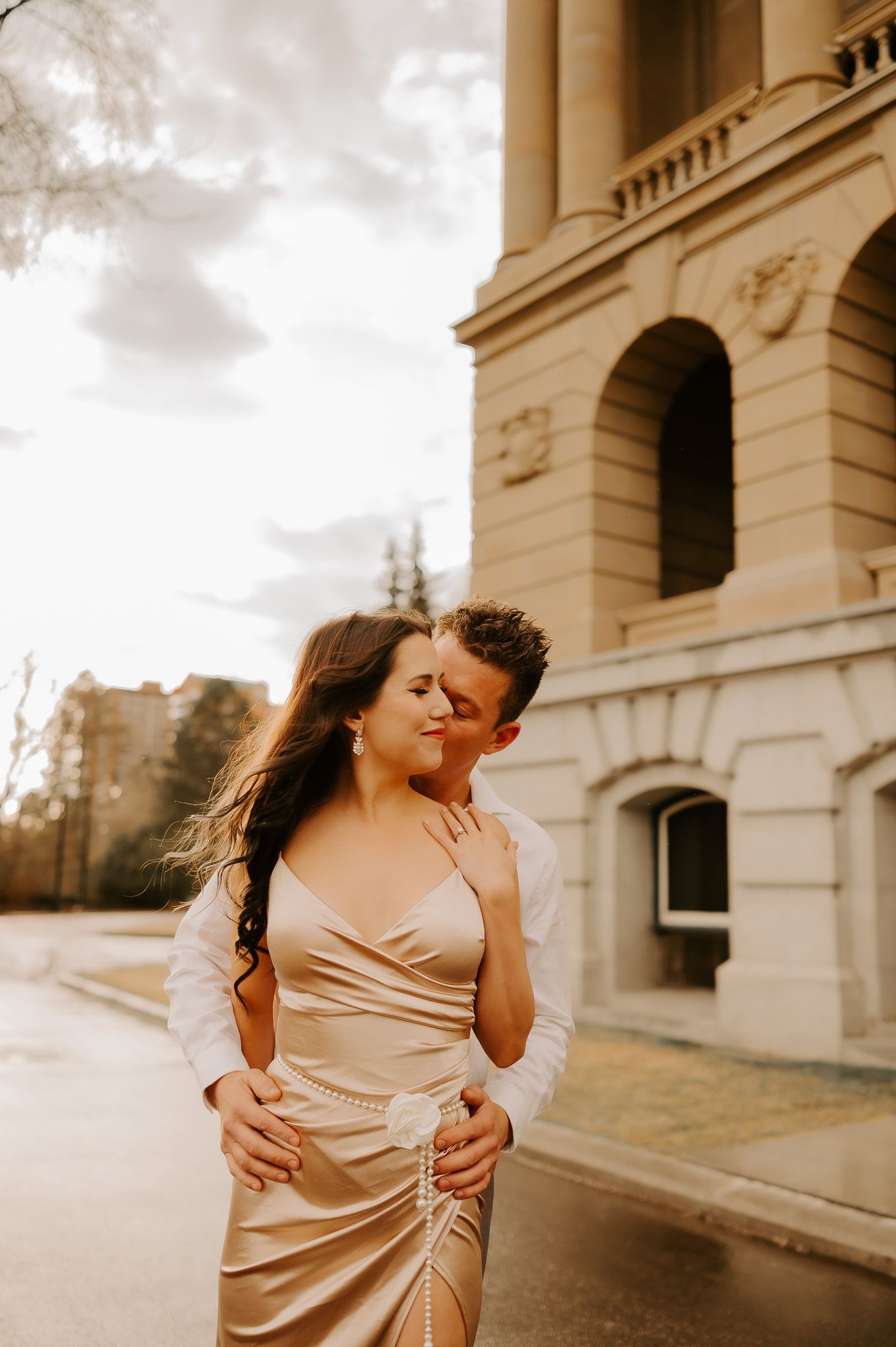 A man and a woman are kissing in front of a building.