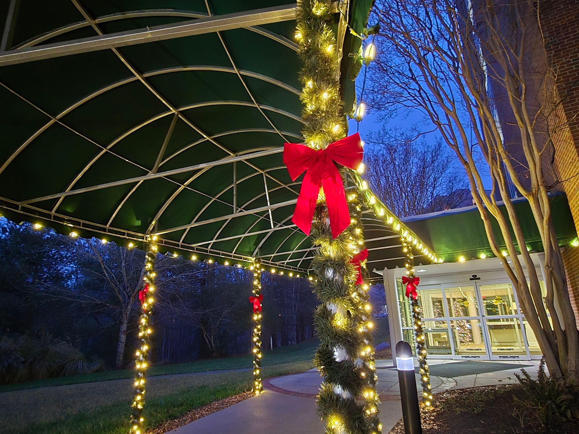 A walkway with green awning decorated with lights and red bows for the holidays.