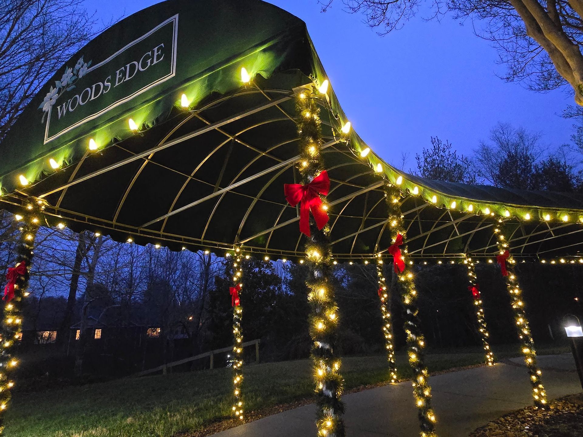 Canopy entrance decorated with lights and bows, leading to Woods Edge at dusk.