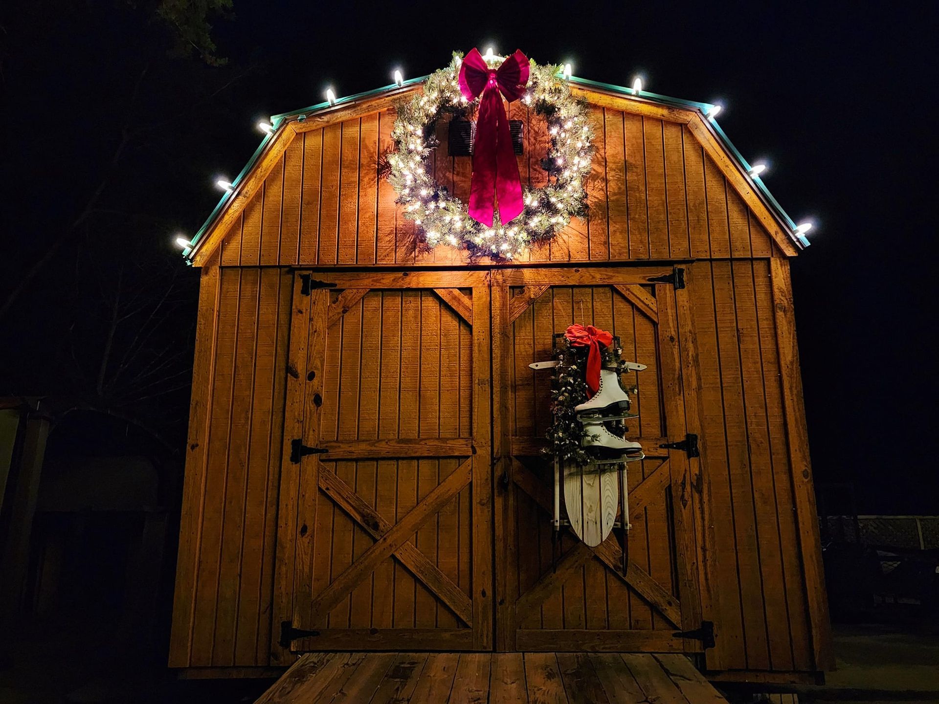 Wooden shed decorated for Christmas with wreath, lights, and sled.