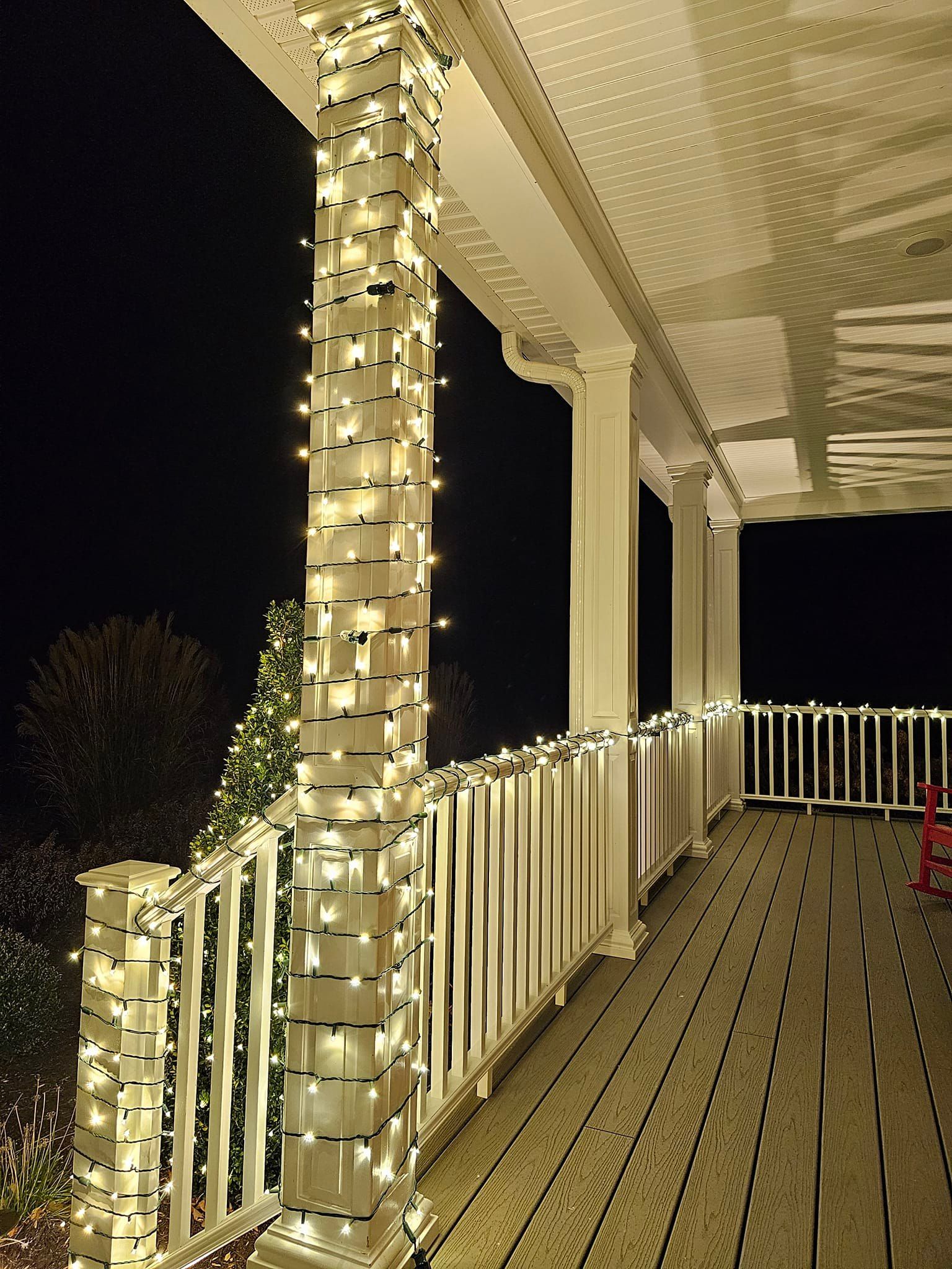 A porch decorated with white Christmas lights, wrapping columns and railing, against a dark night sky.