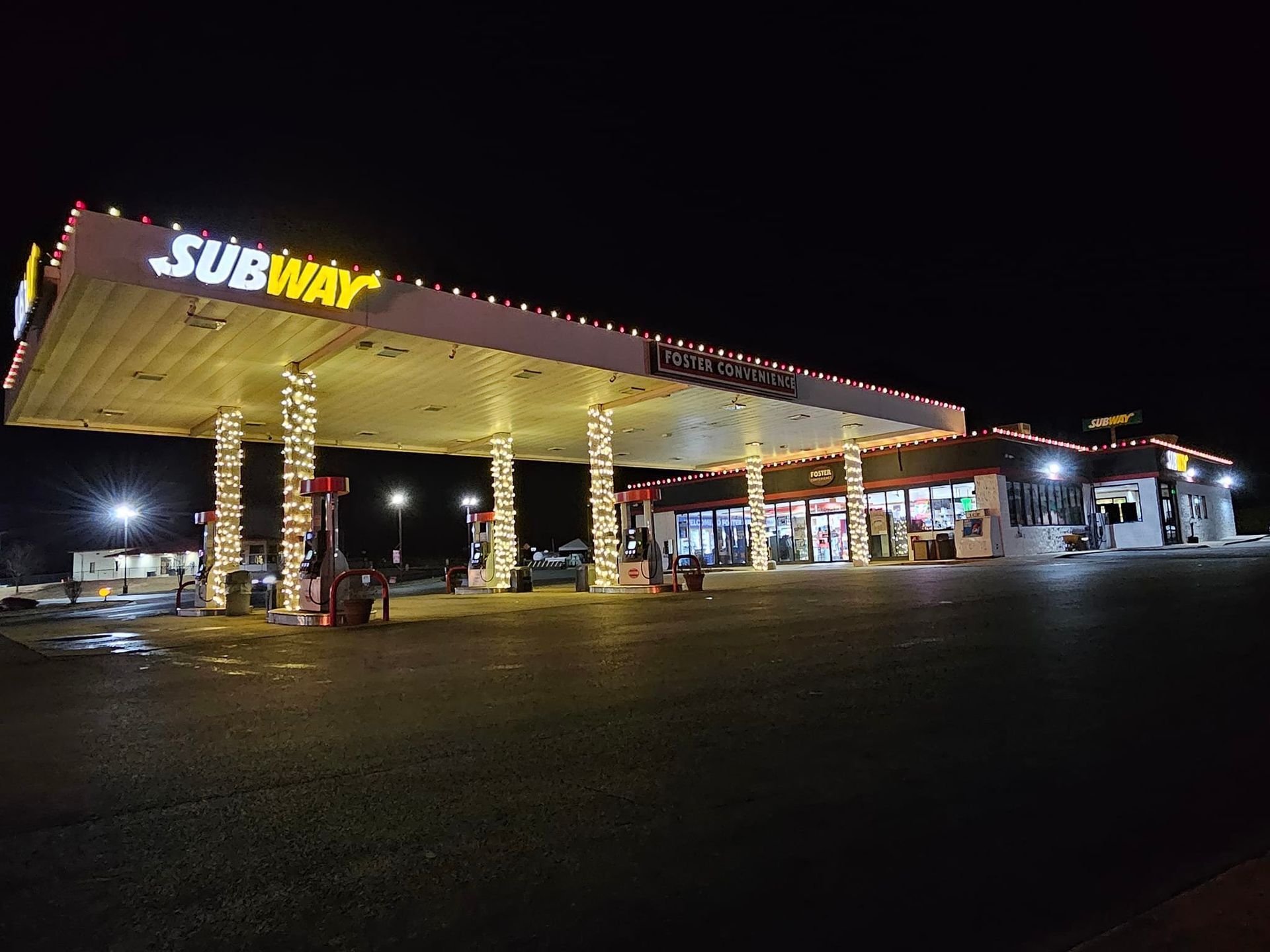Gas station at night, lit with string lights. Subway sign visible.