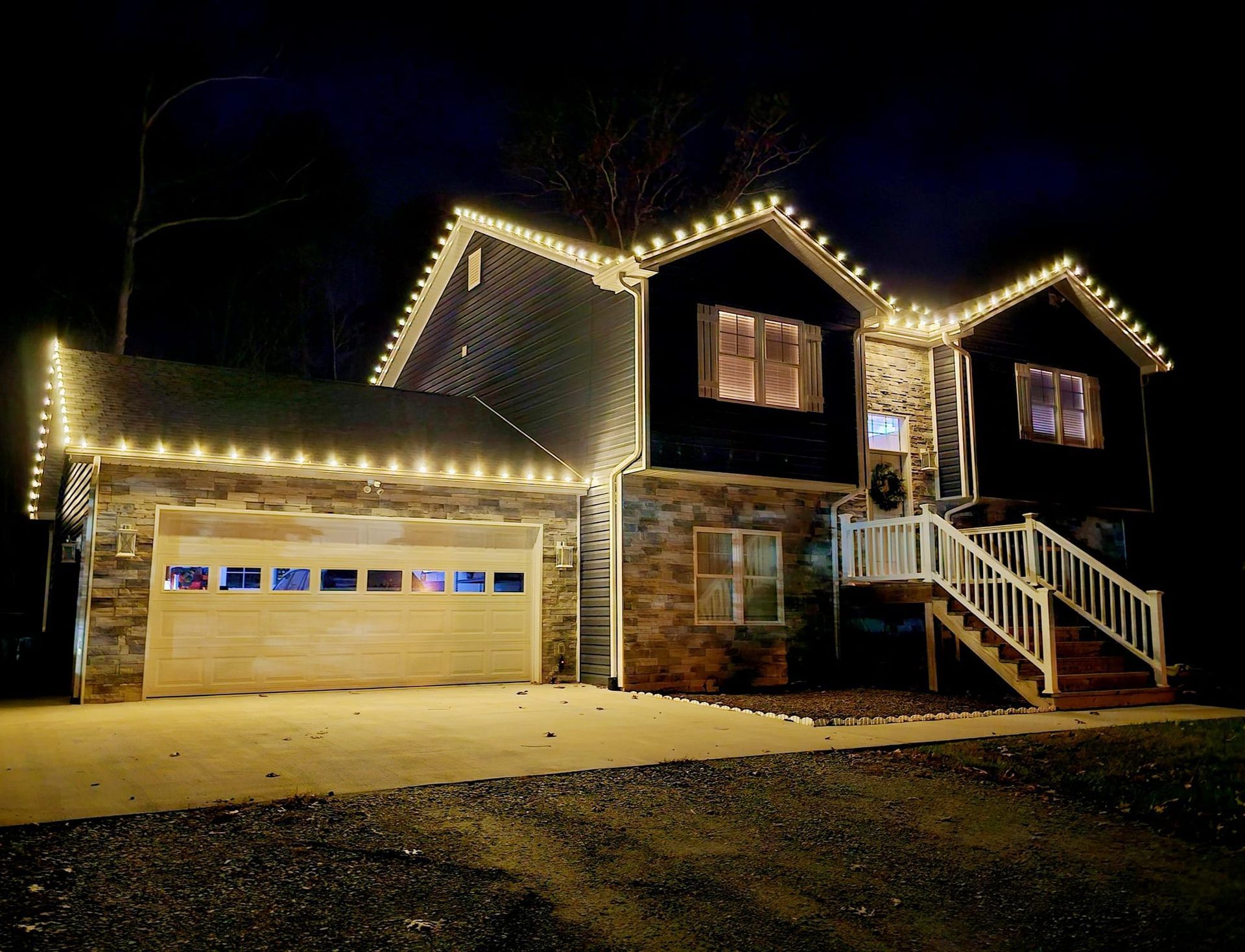 House at night with warm white Christmas lights outlining roof and garage.