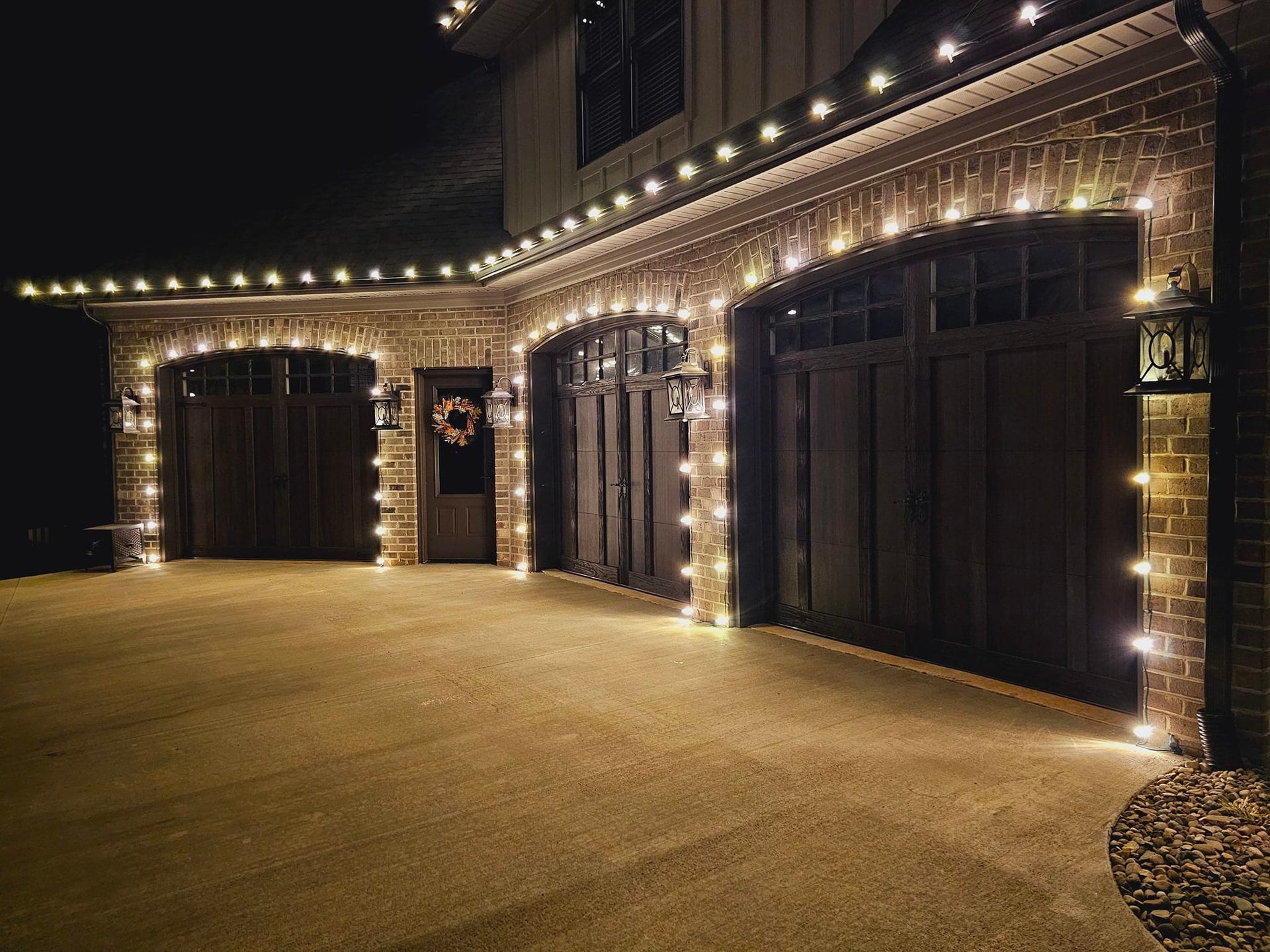 Garage doors with white lights, lit at night. Brick exterior with a wreath on the door.