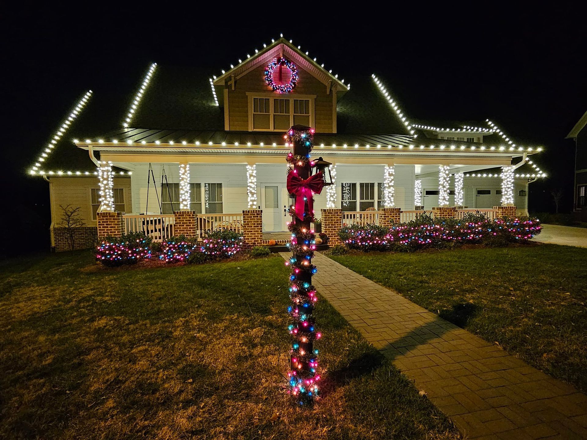 Festive house at night, adorned with Christmas lights and a decorated pole in the front yard.
