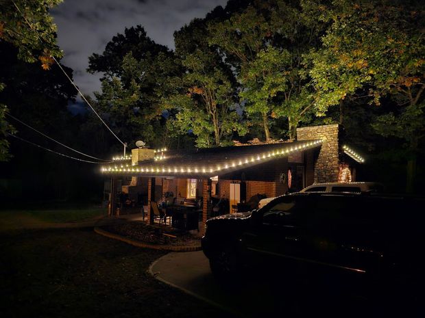 Cabin at night with string lights, trees, and car in the foreground.