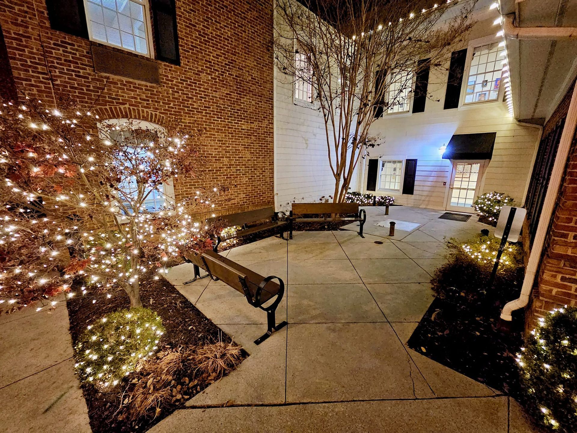 Courtyard at night, brick buildings and benches, decorated with string lights.