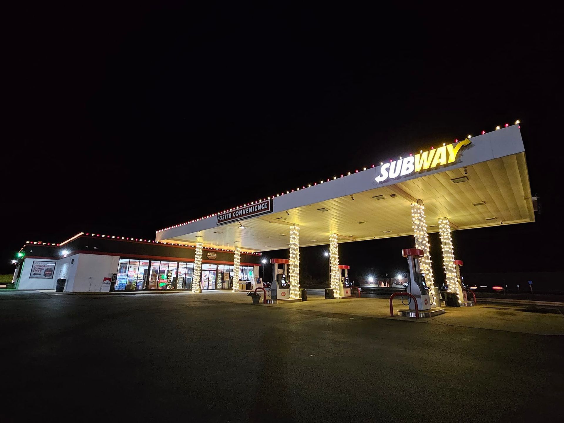 Gas station at night, decorated with white lights, Subway sign visible.