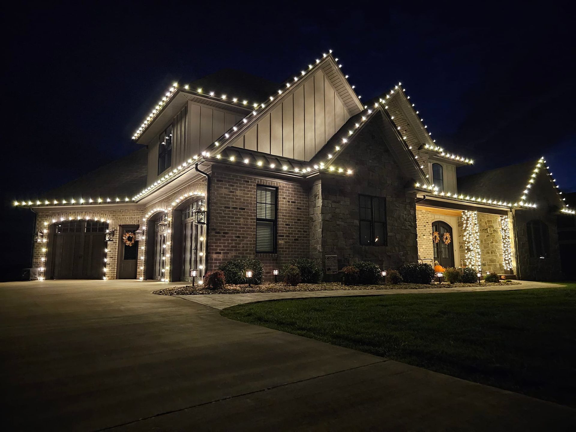 A house illuminated with white Christmas lights along the roof and entryway at night.