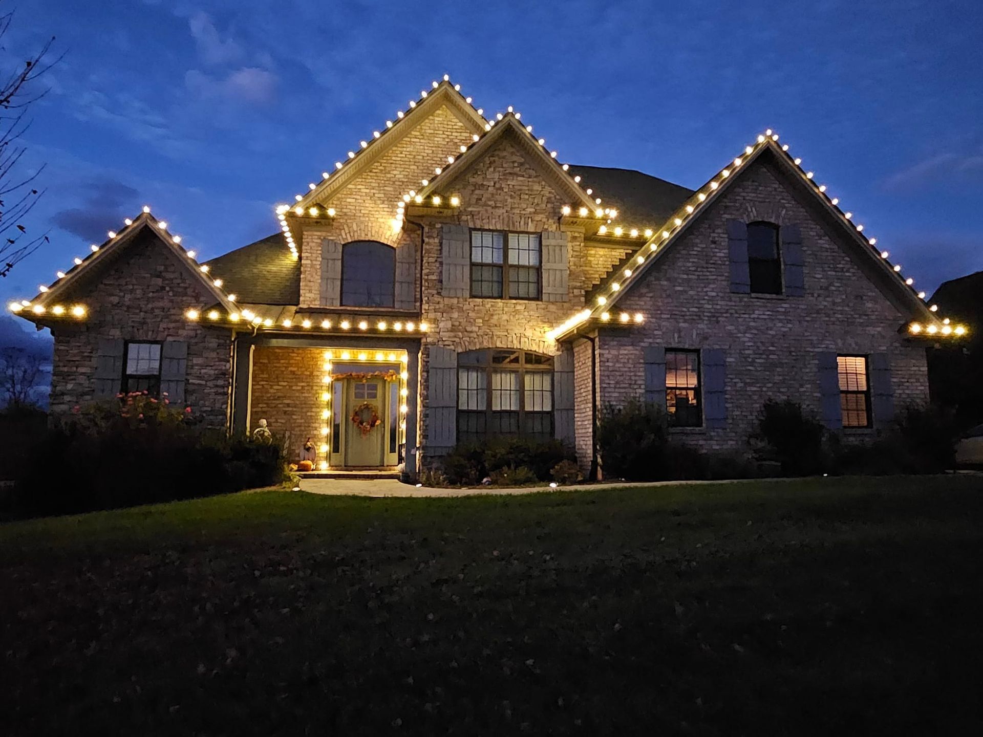 House with white Christmas lights outlining roof and windows against a twilight sky.