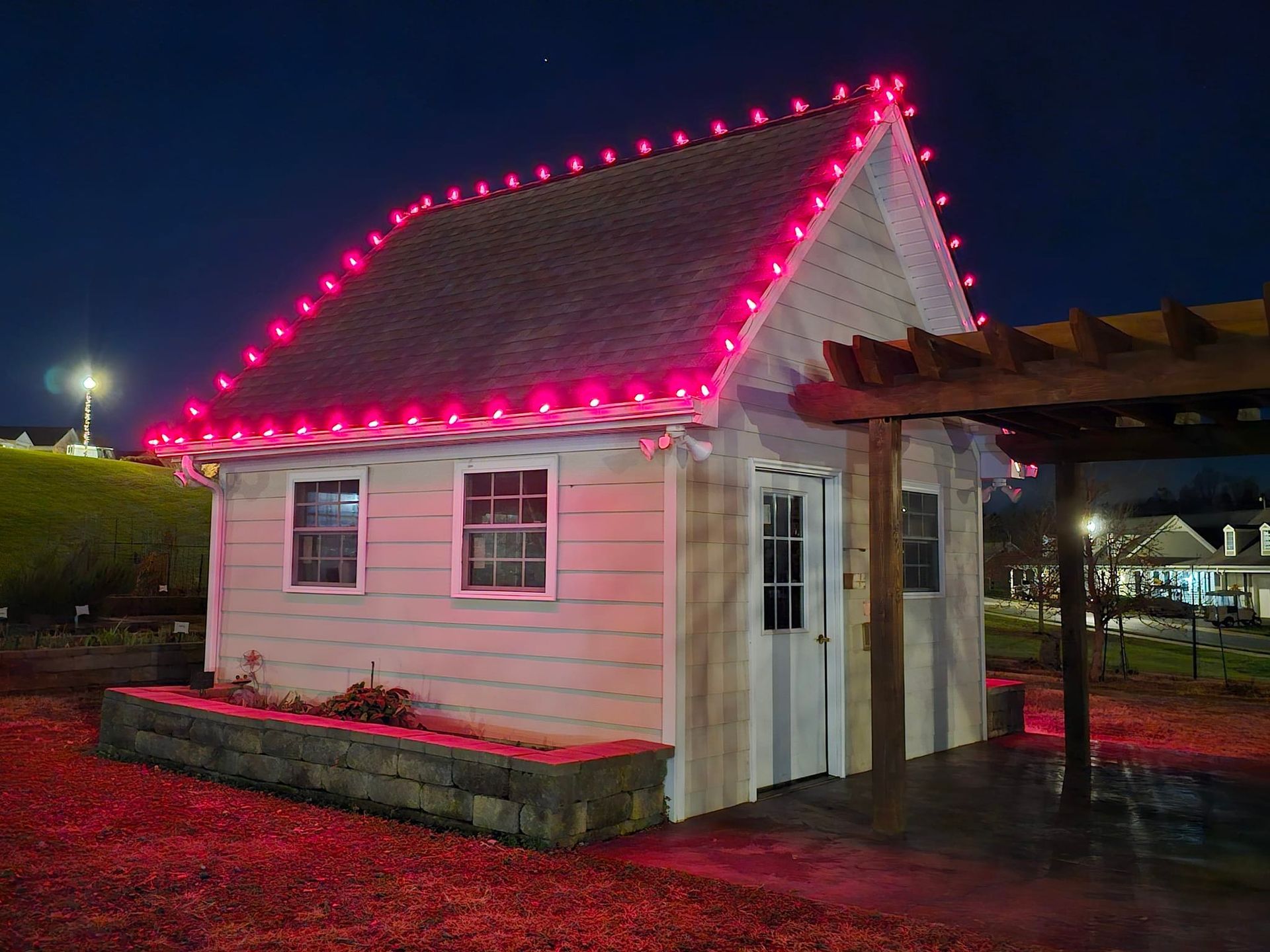 Small white building with a pink light-lined roof, windows, and door. Illuminated at night.