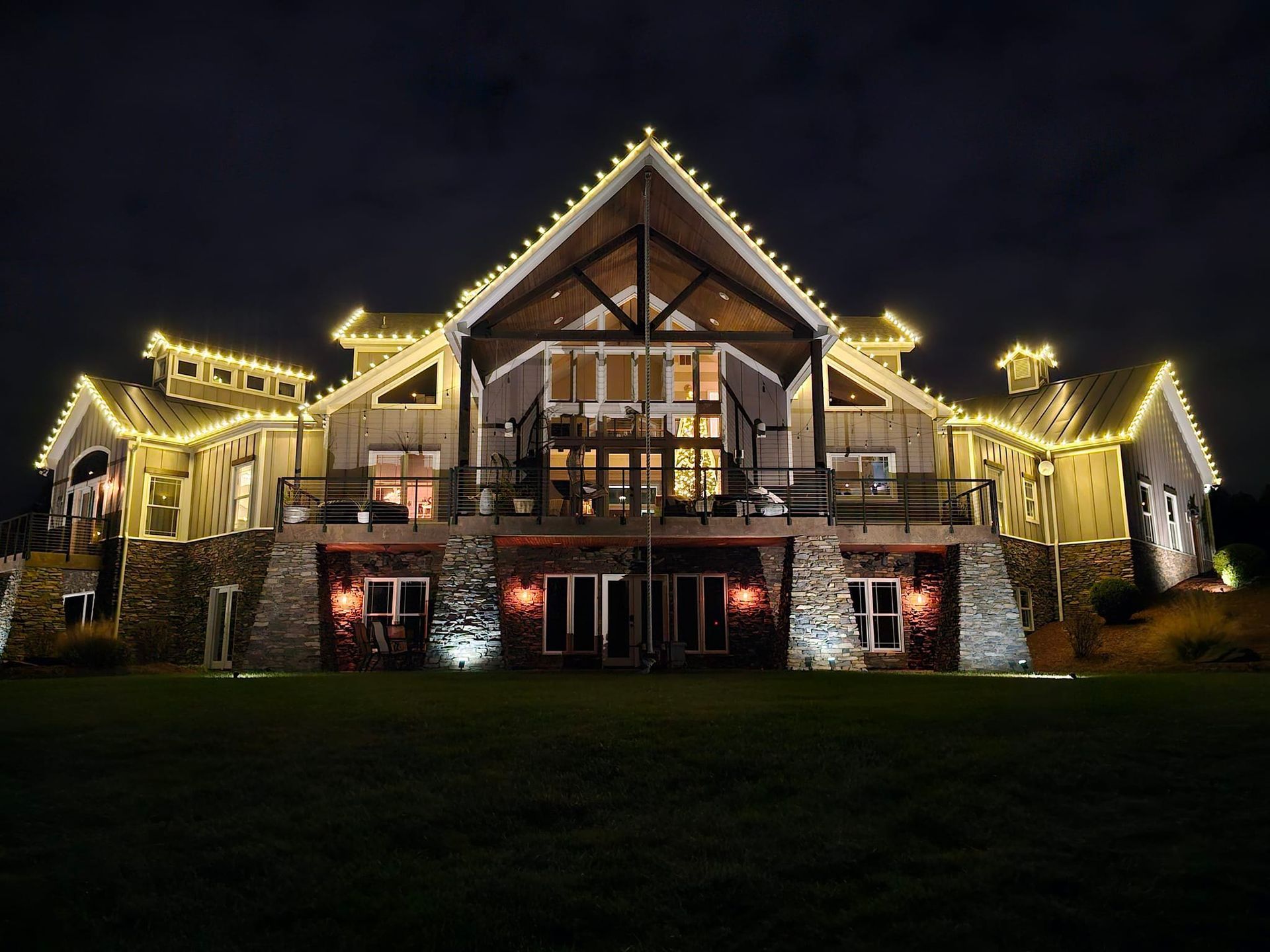 Large, rustic building at night, lit with yellow string lights; stone base, dark sky.