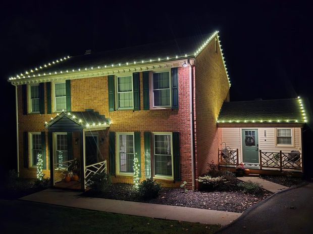 Brick house and cottage lit with white Christmas lights at night.