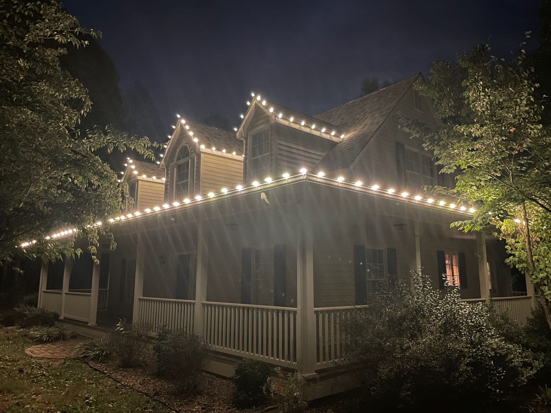 House at night with roofline illuminated by white string lights.