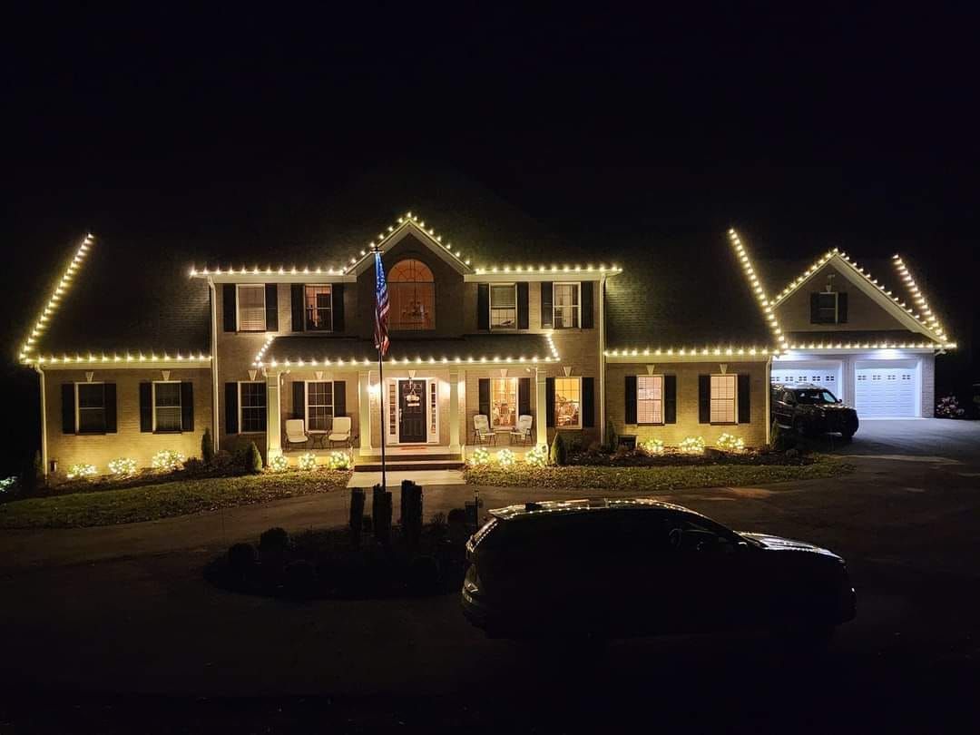 House at night decorated with white Christmas lights; car parked in front.