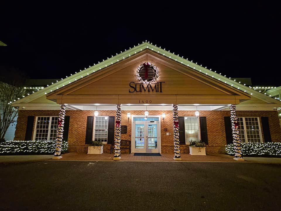 The Summit building entrance at night, decorated with holiday lights. Brick exterior, lit columns