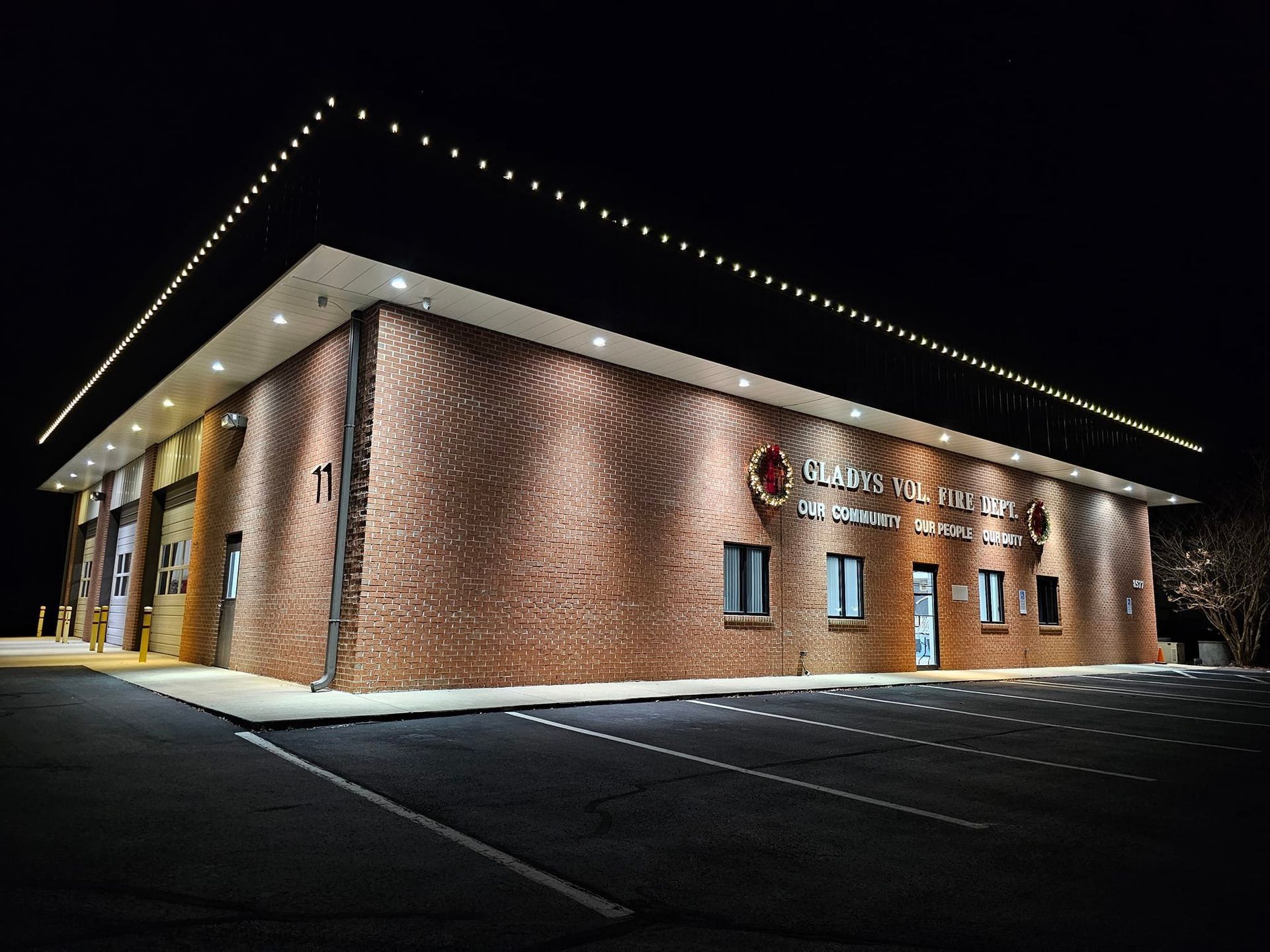 Brick building at night with lit roofline and parking lot.