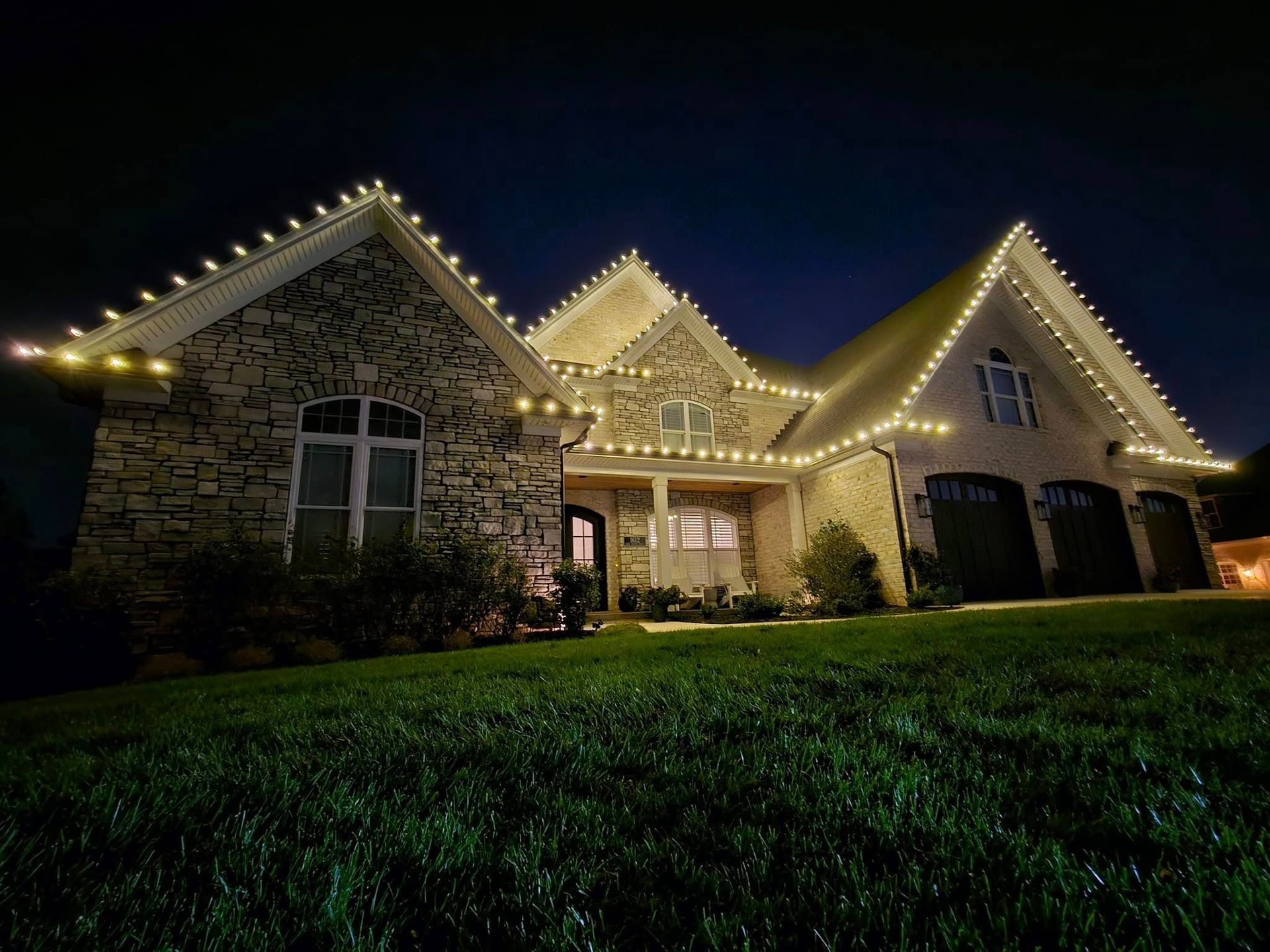 House at night with warm white Christmas lights outlining rooflines.