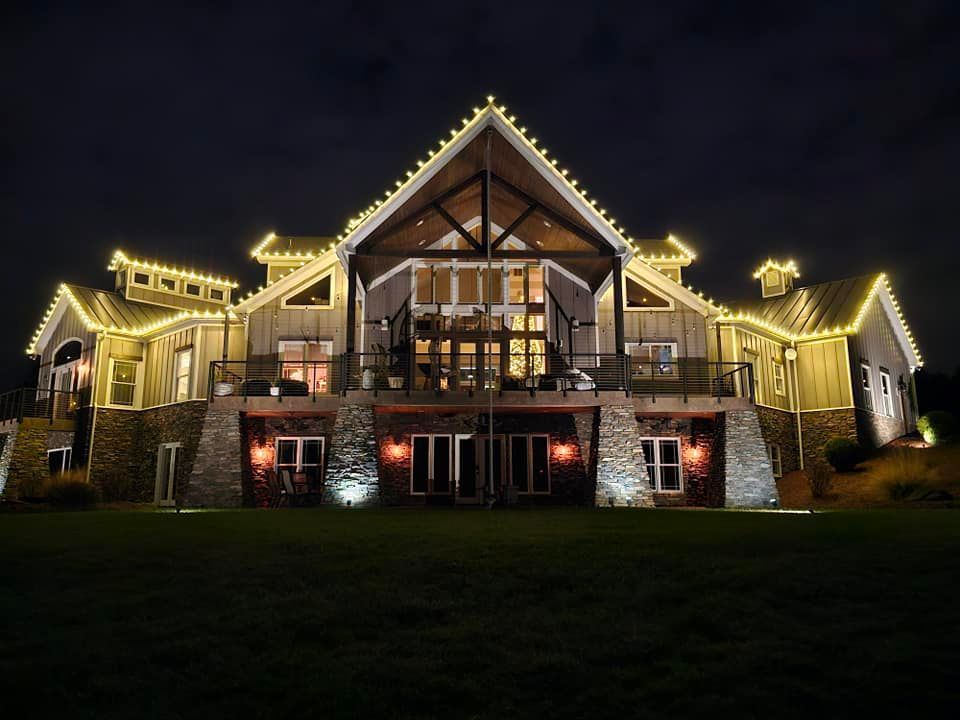 Large house at night, illuminated by yellow lights along the roof. Stone base, large glass doors, dark sky.
