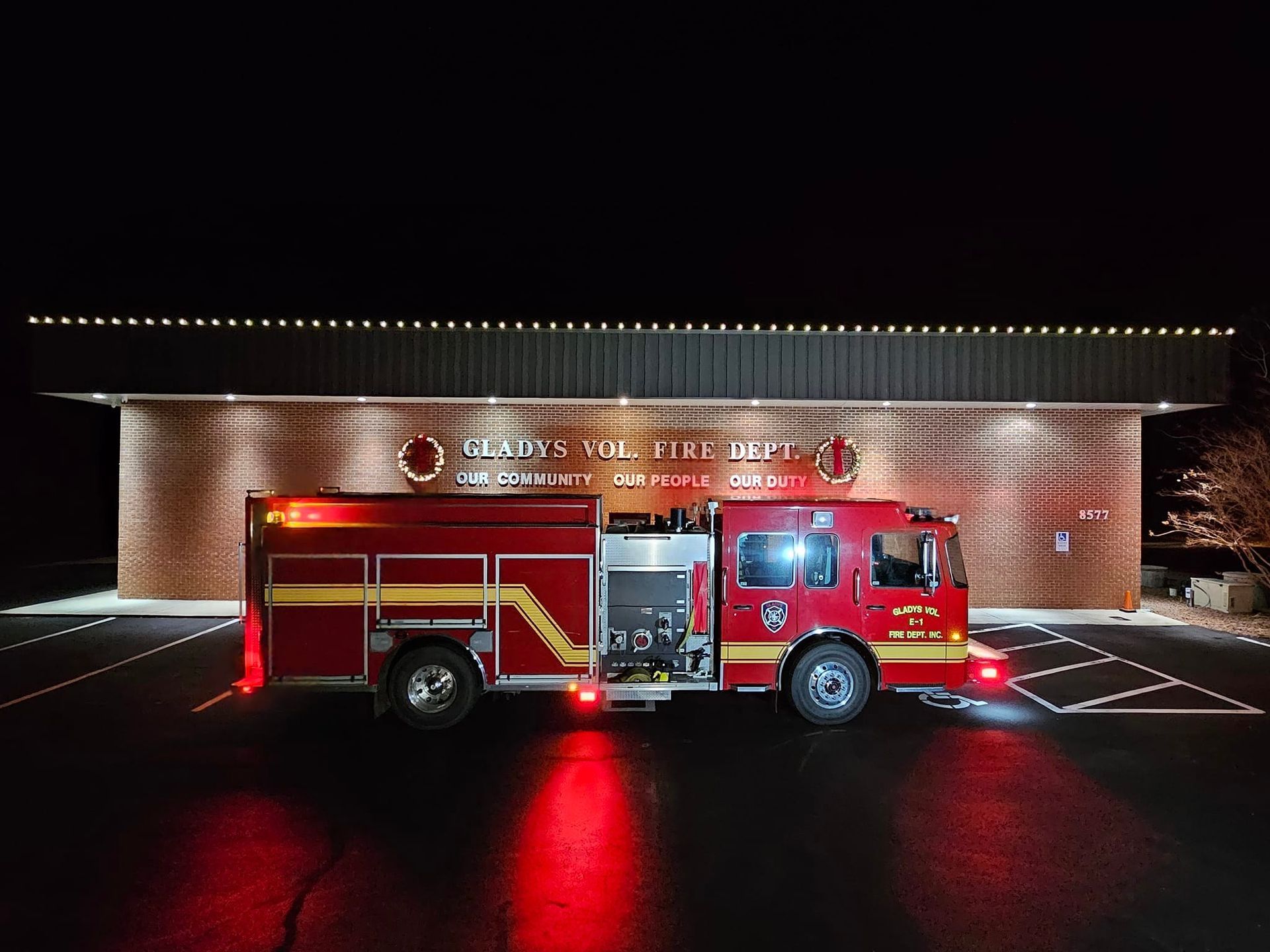 Fire engine parked in front of a brick fire station at night, lights on.