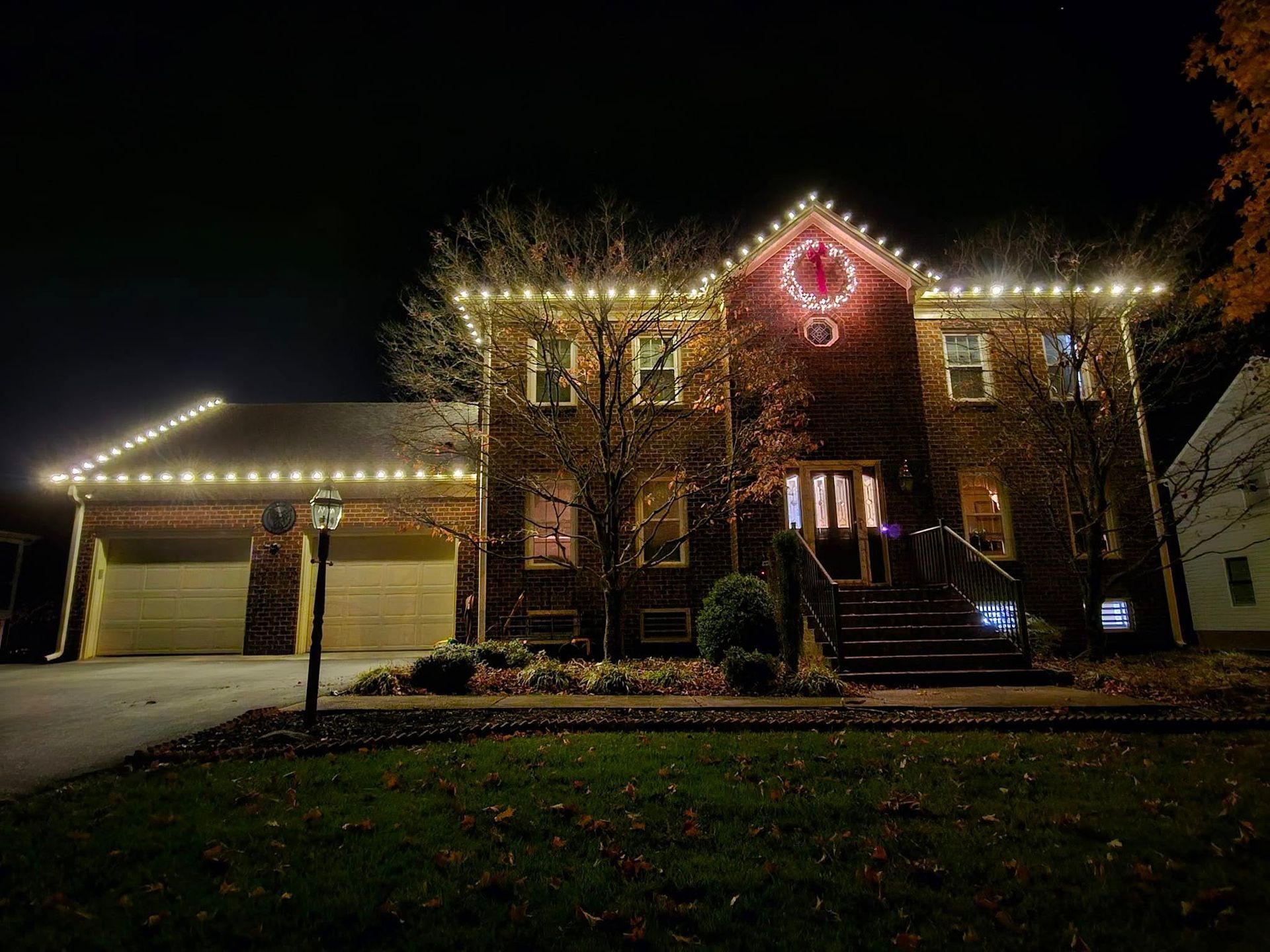 A two-story brick house at night, illuminated with white Christmas lights along the rooflines.