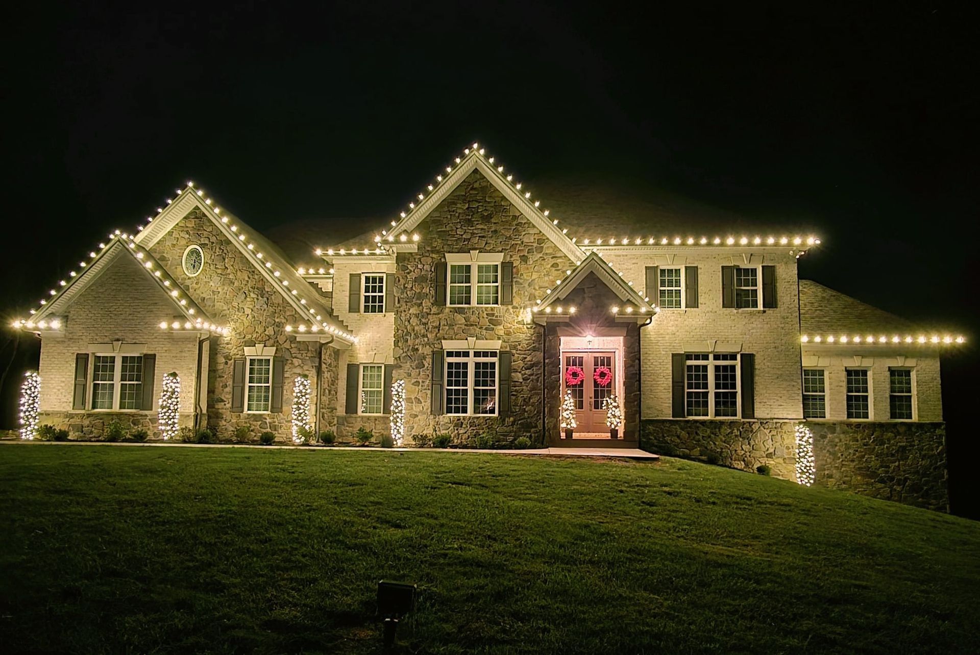 A large house at night, illuminated with white Christmas lights along the roof and windows; a Christmas