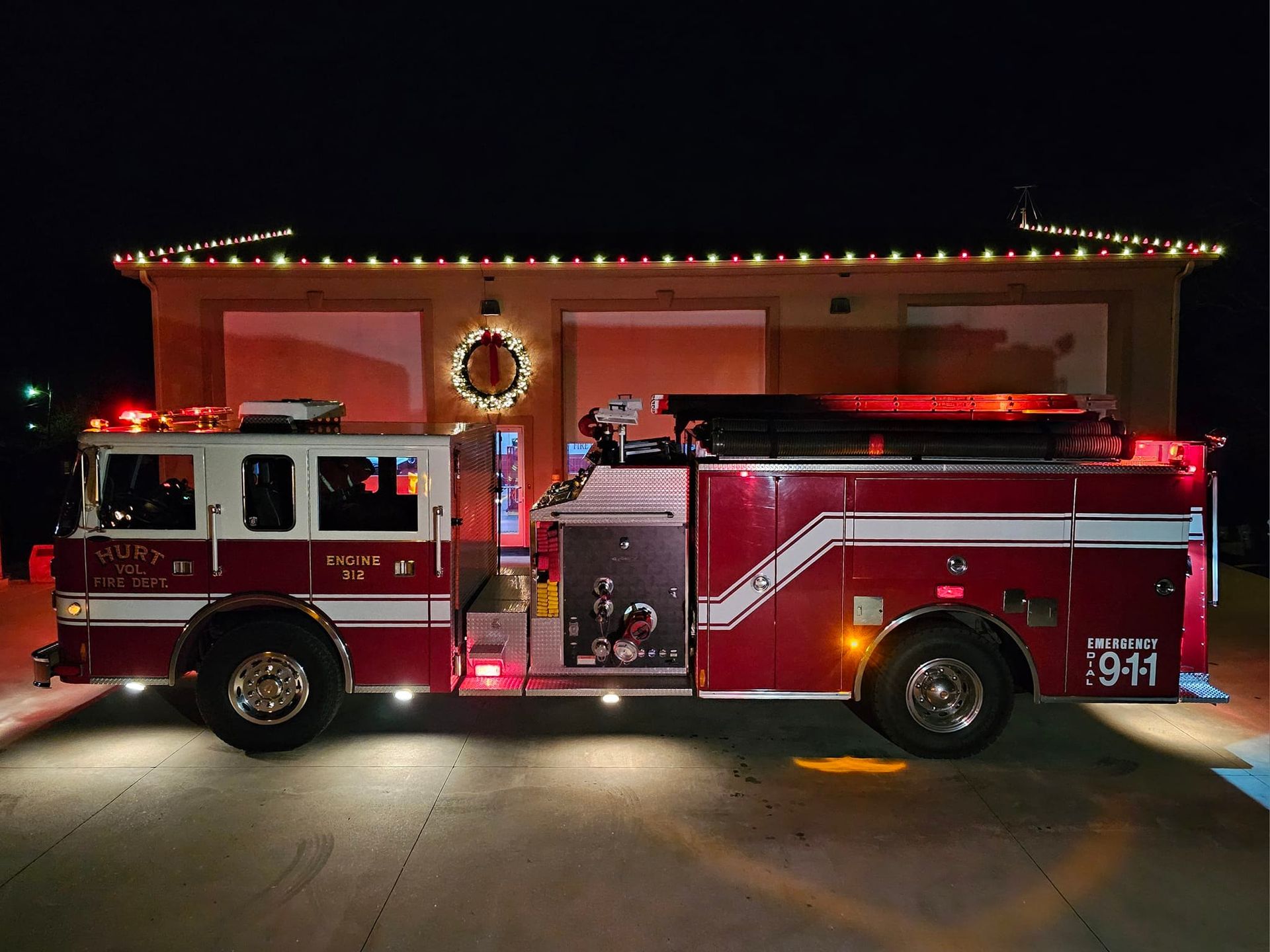 Fire engine in front of a station decorated with Christmas lights at night.