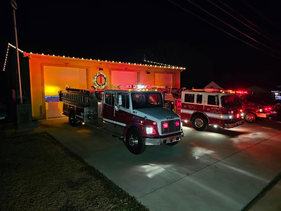 Fire trucks parked outside a building at night. Lights are on, and the building is decorated.