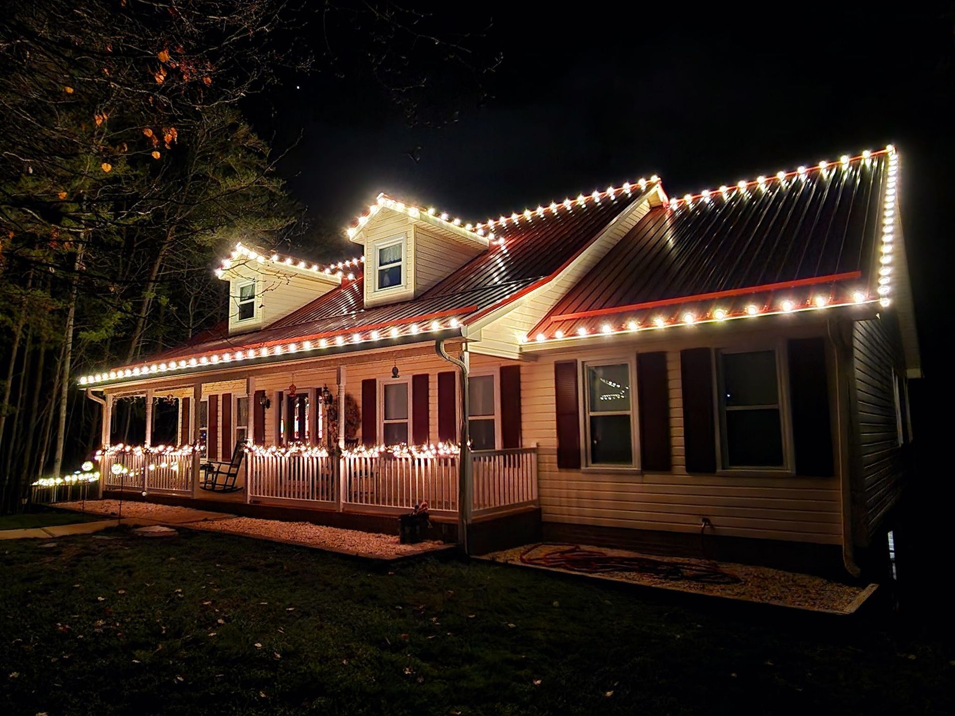 House decorated with white Christmas lights on the roof and porch at night.