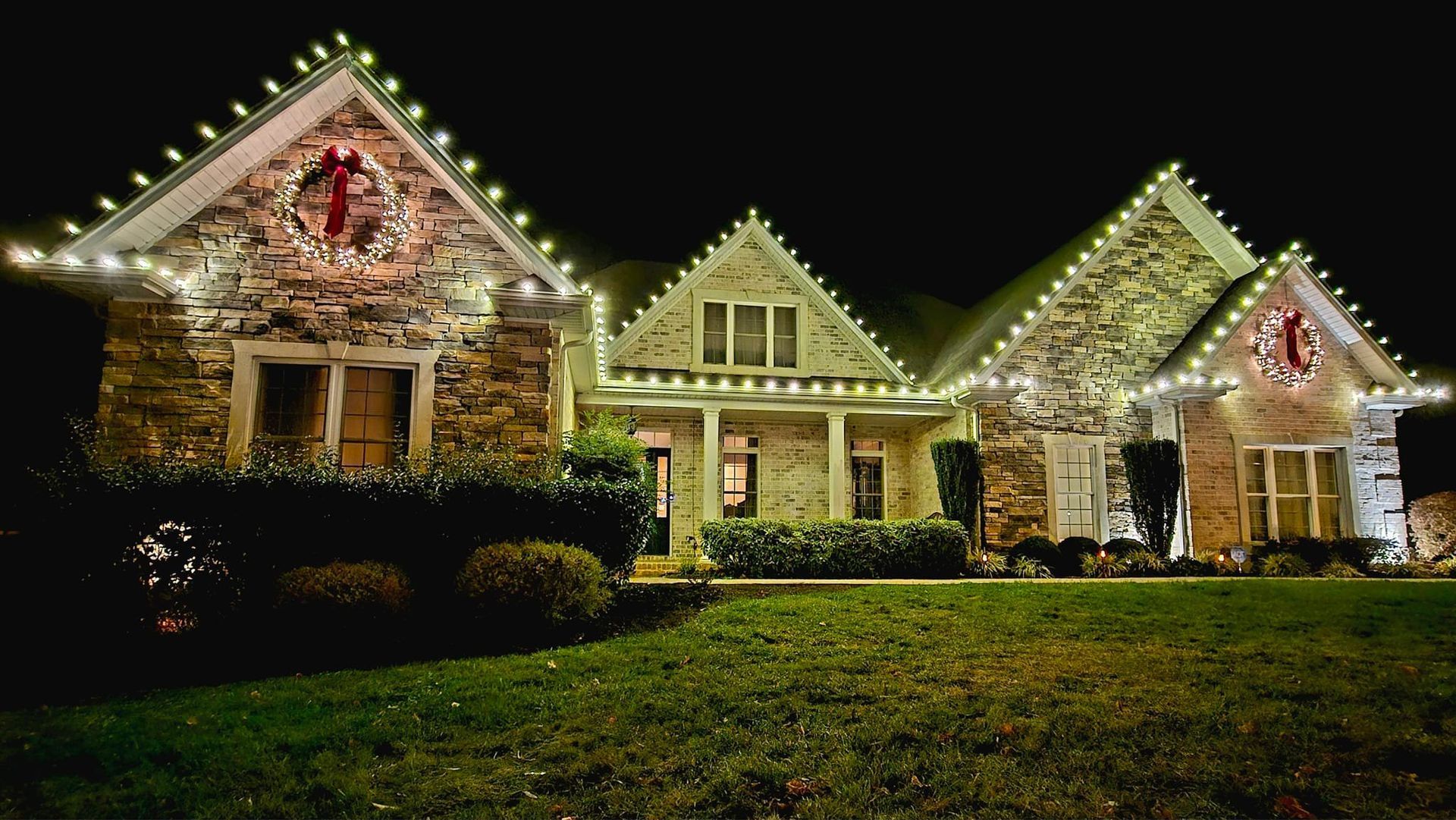 House with holiday lights and wreaths at night.