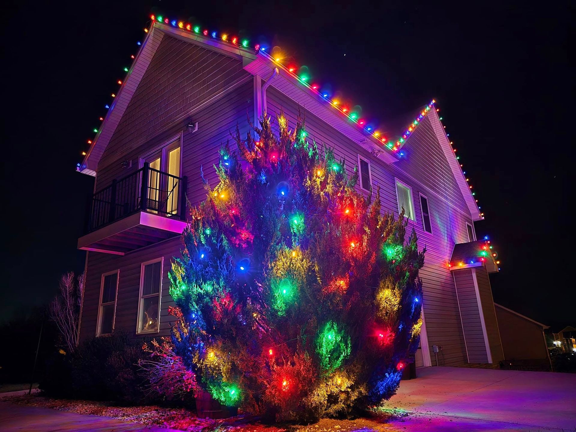 House and bush brightly decorated with colorful Christmas lights at night.