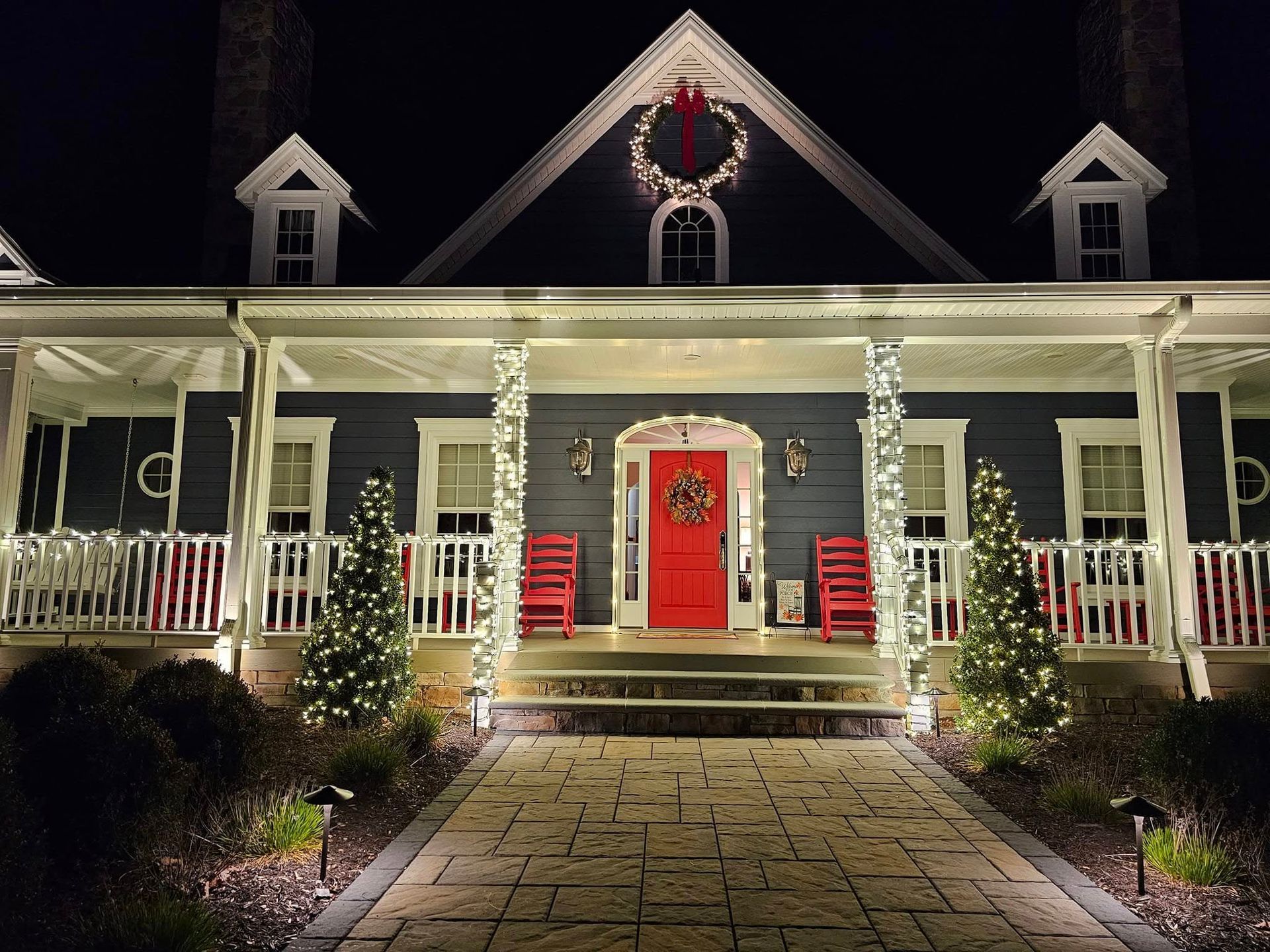 A house at night, decorated for Christmas with lights, a wreath, and red accents.