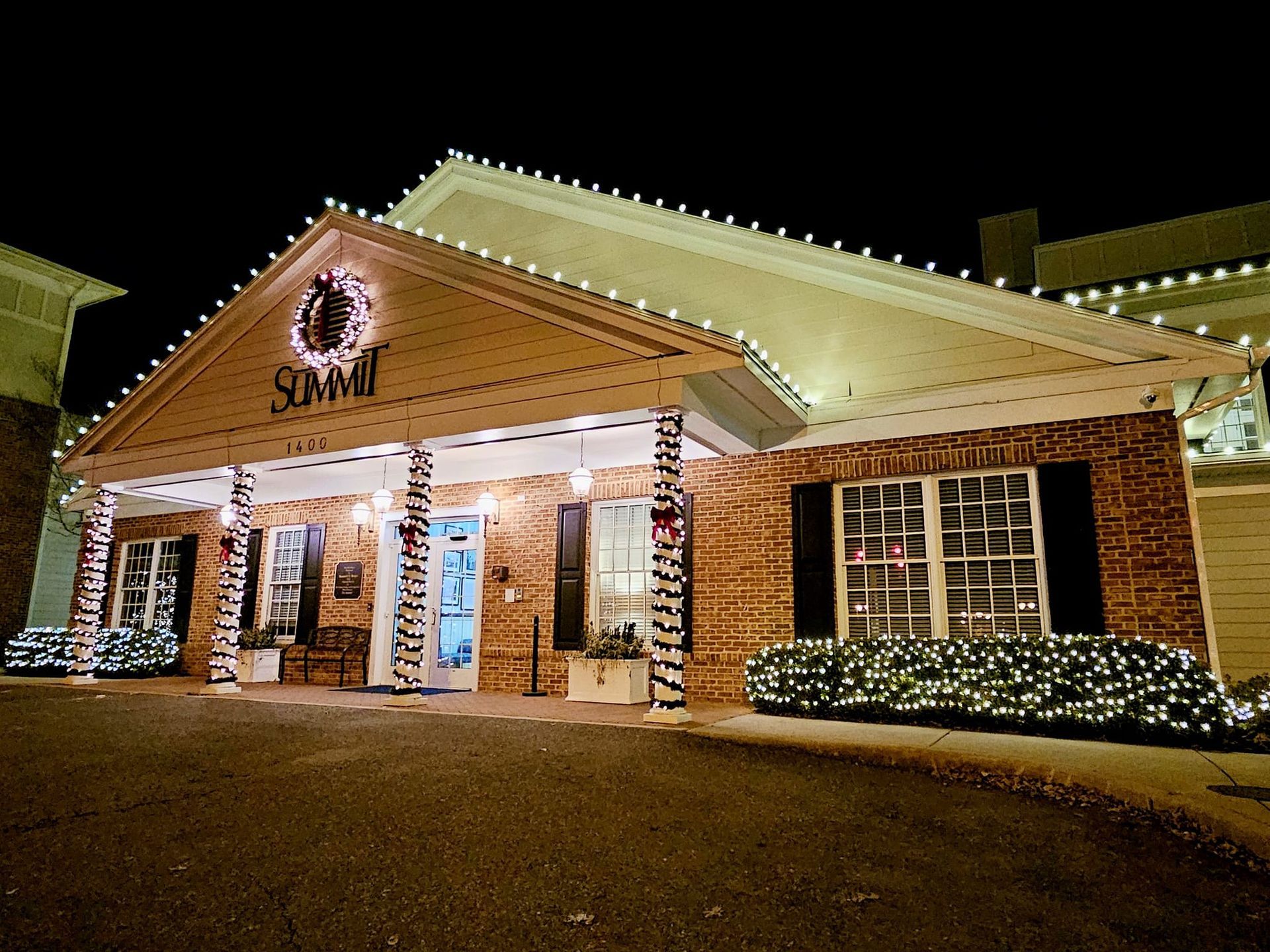 Brick building lit with Christmas lights; Summit sign over the door, lit garland around columns and windows.