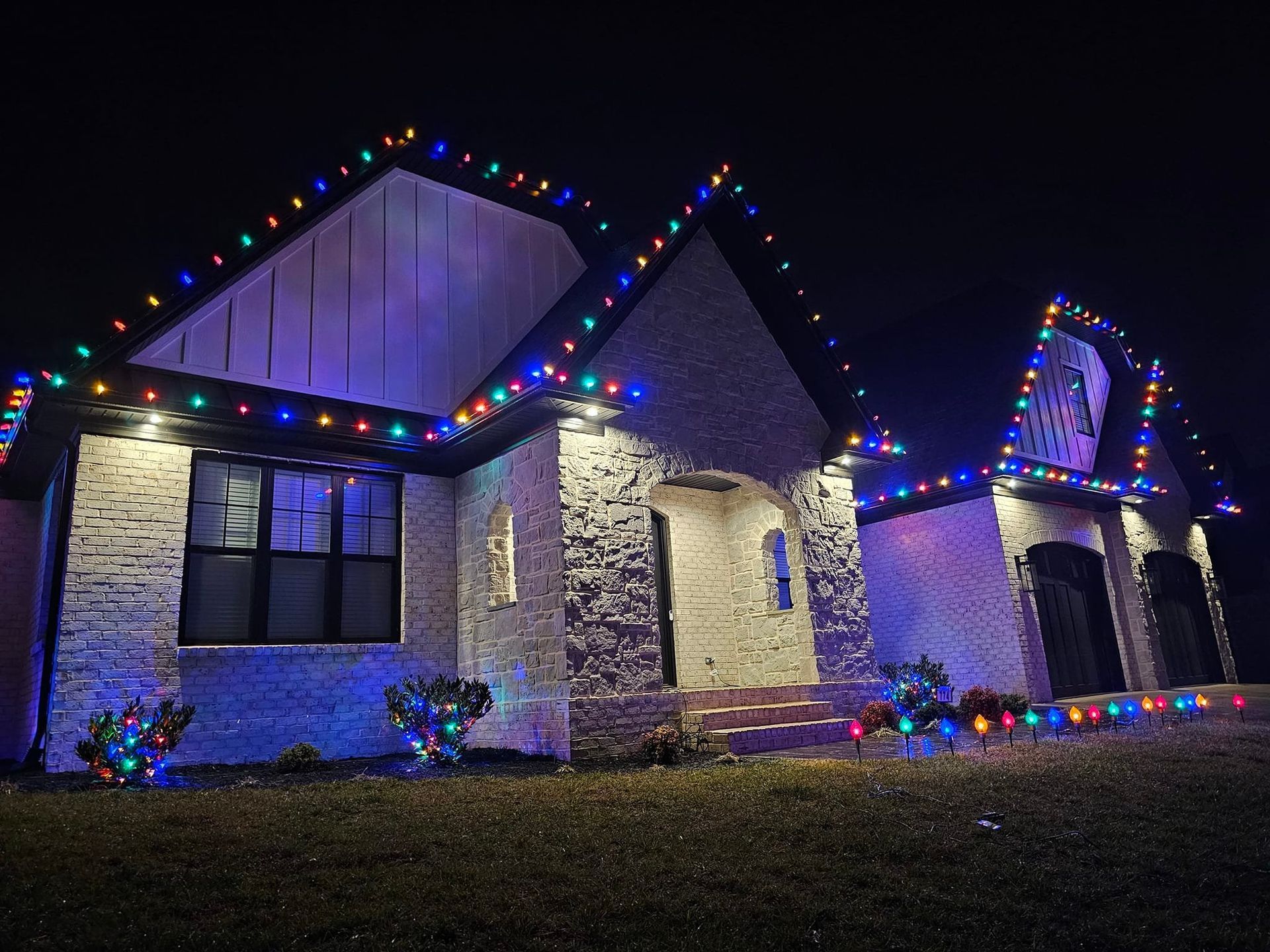 House with brick facade and colorful Christmas lights, night setting.
