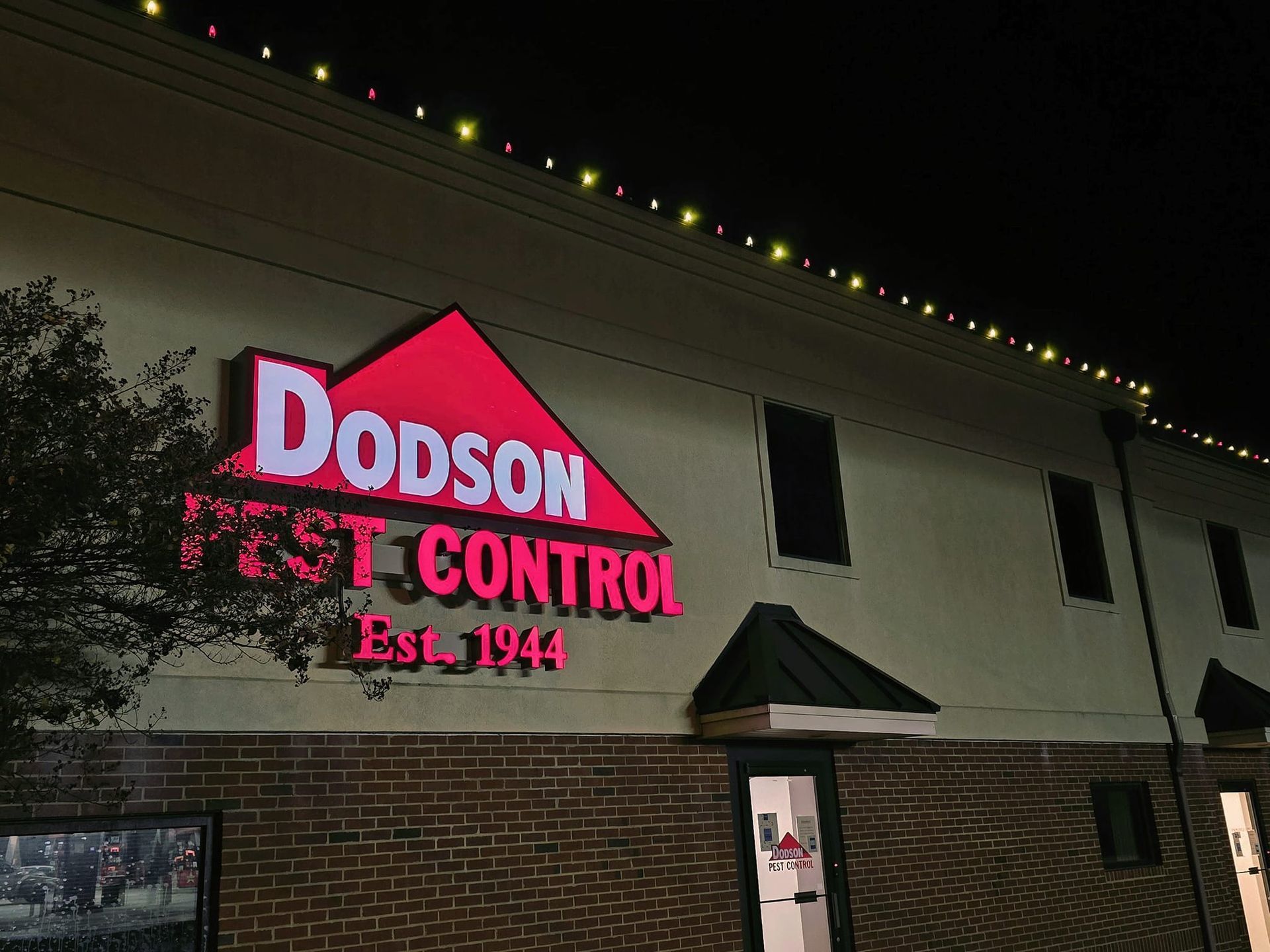 Dodson Pest Control sign on a building at night. Red and white lettering on a tan brick building. Established 1944.