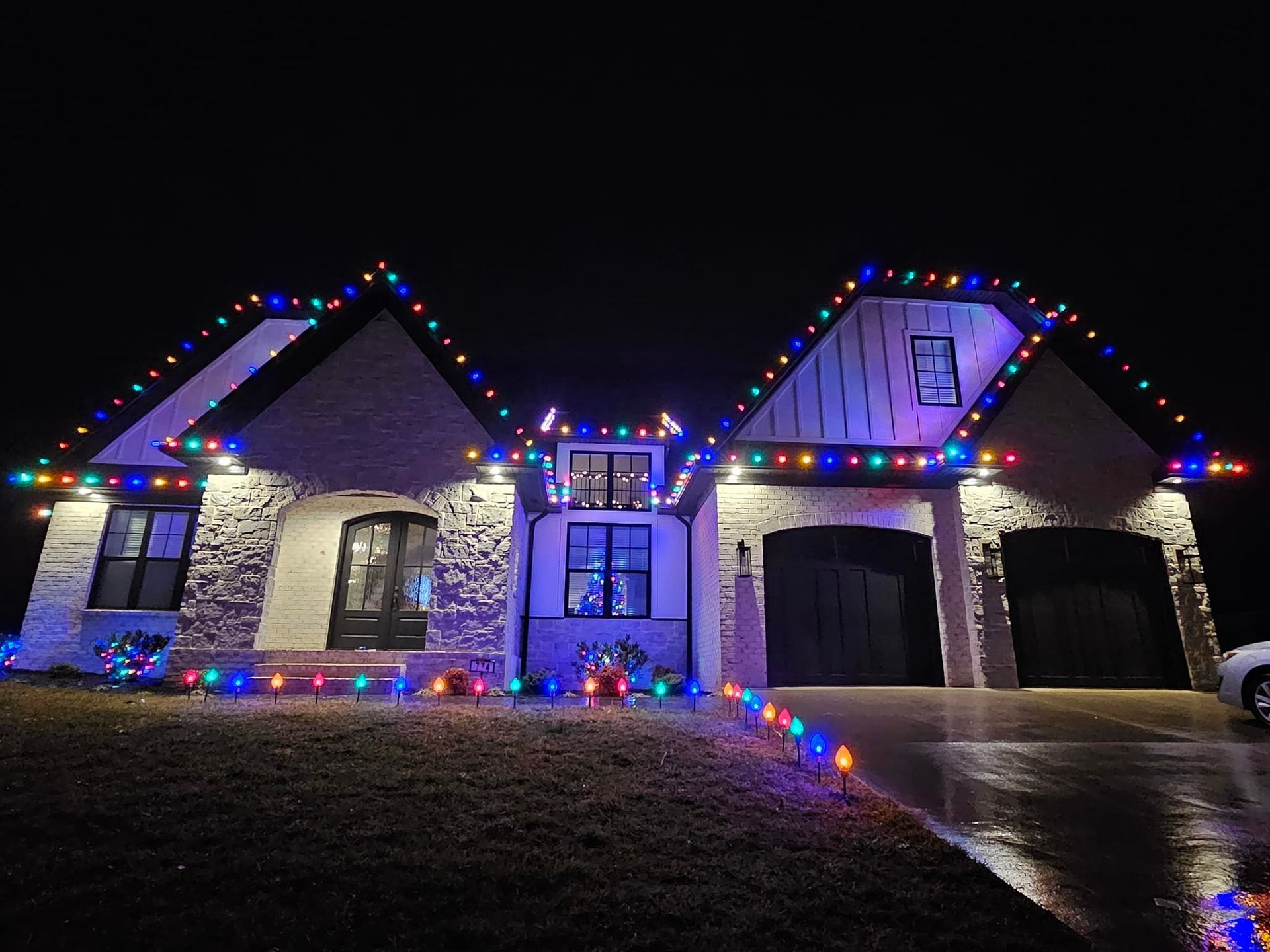A house at night with colorful Christmas lights outlining the roof and ground.