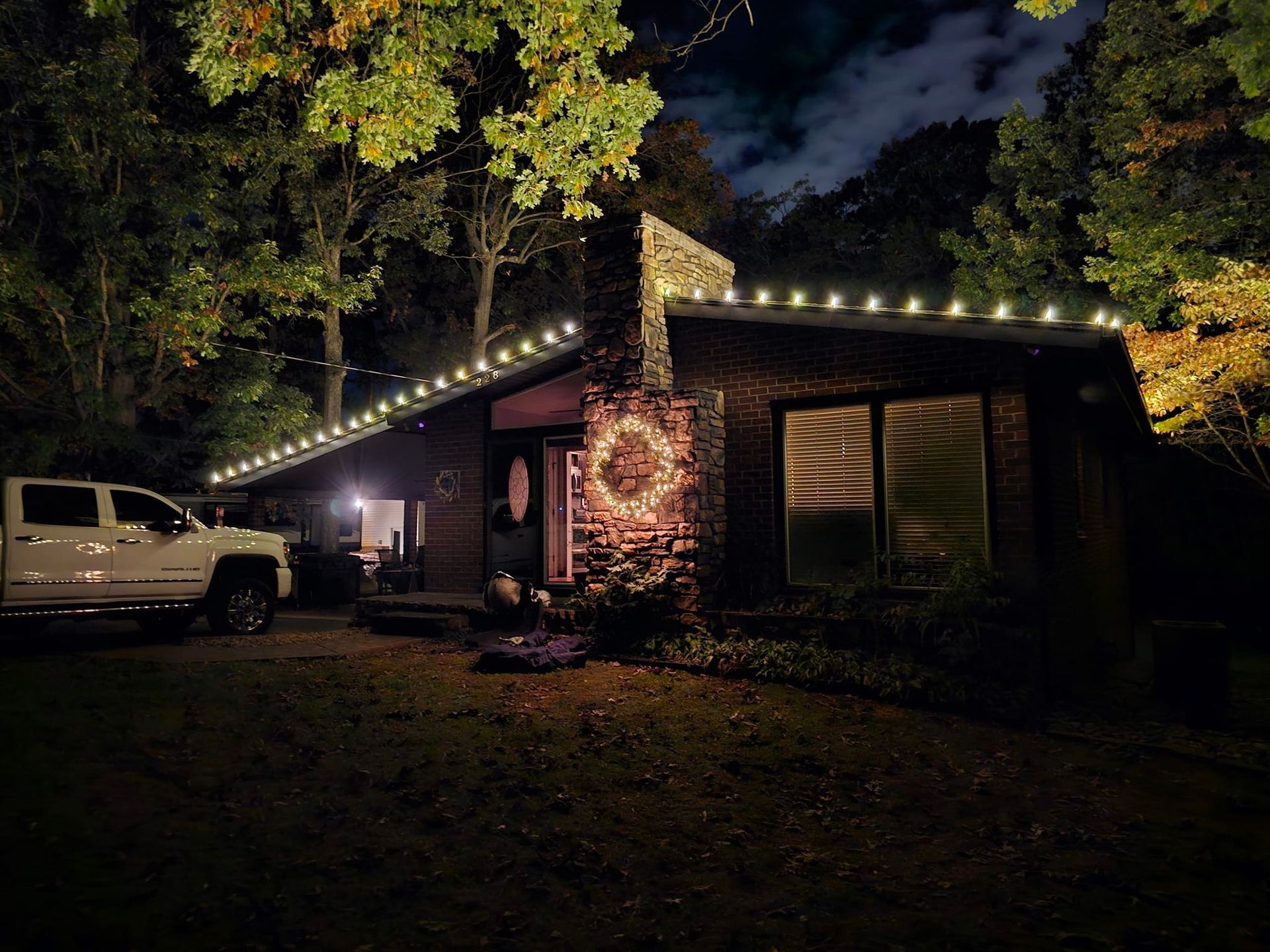 House at night with Christmas lights, white truck, and illuminated wreath.