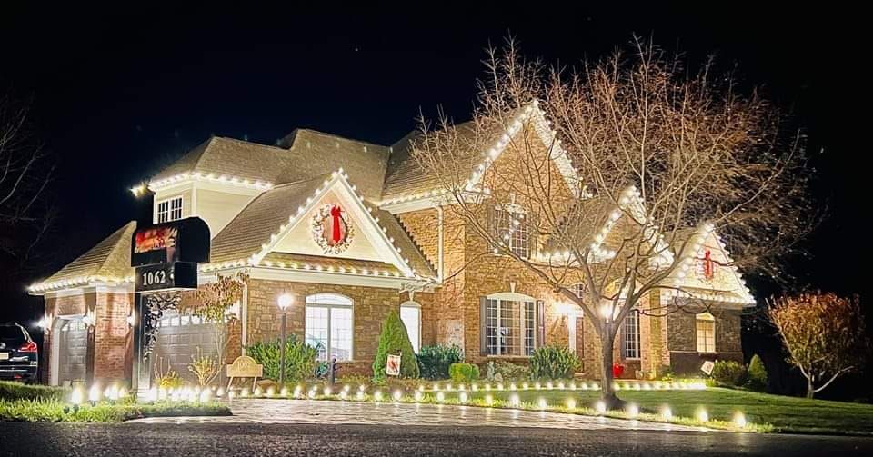 A brick house at night, decorated with white Christmas lights along the roof and the lawn.