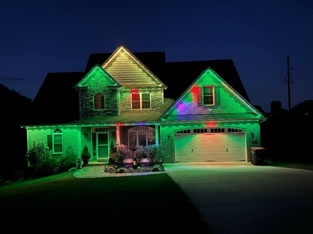 A house illuminated with green lights and a few red and purple spots against a dark blue sky.