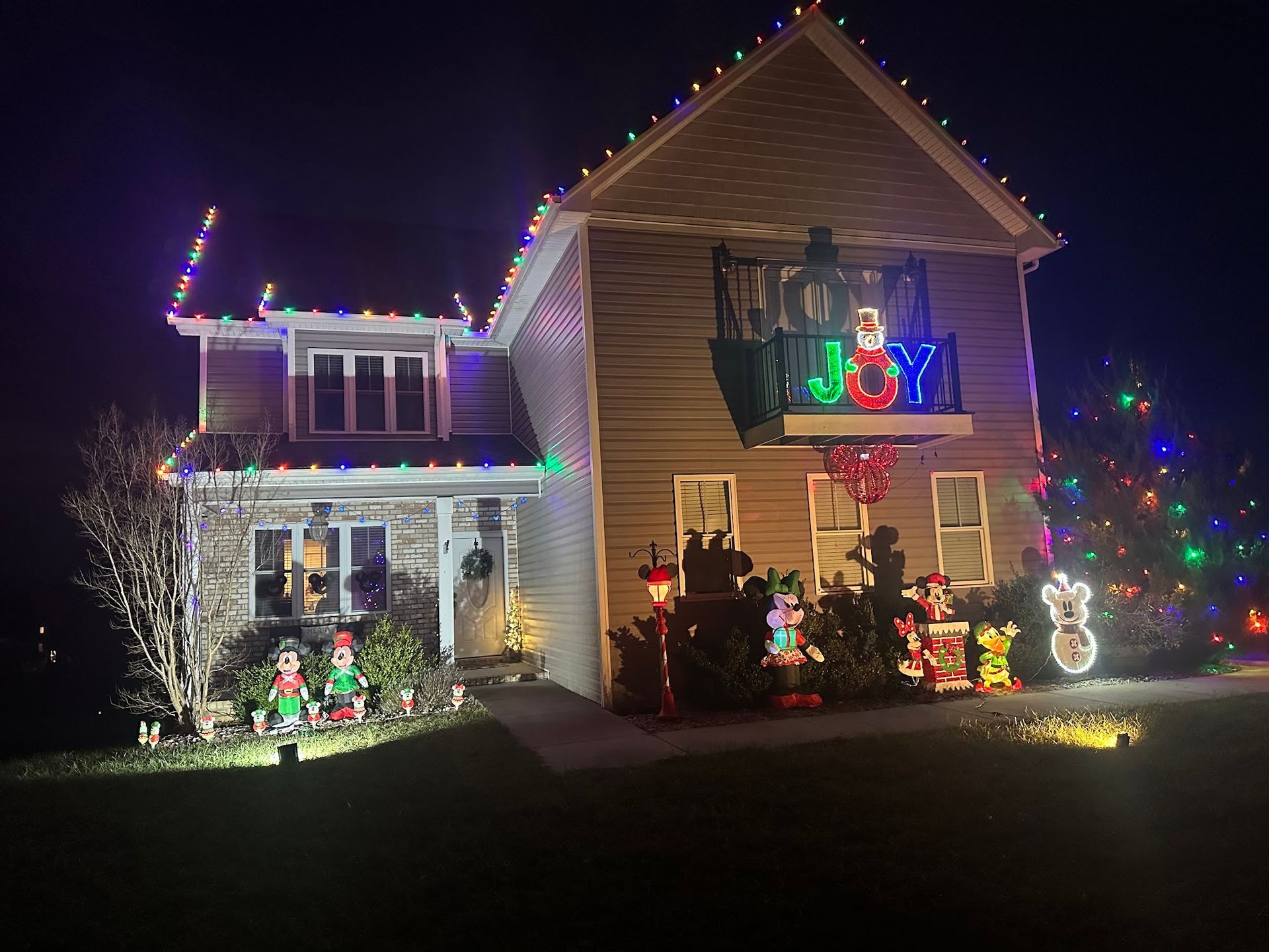 House decorated for Christmas with lights and festive displays, including “JOY” sign.