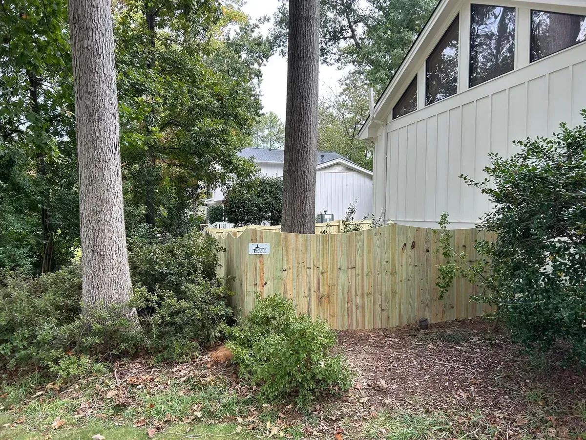 A wooden fence is surrounded by trees and bushes in front of a house.