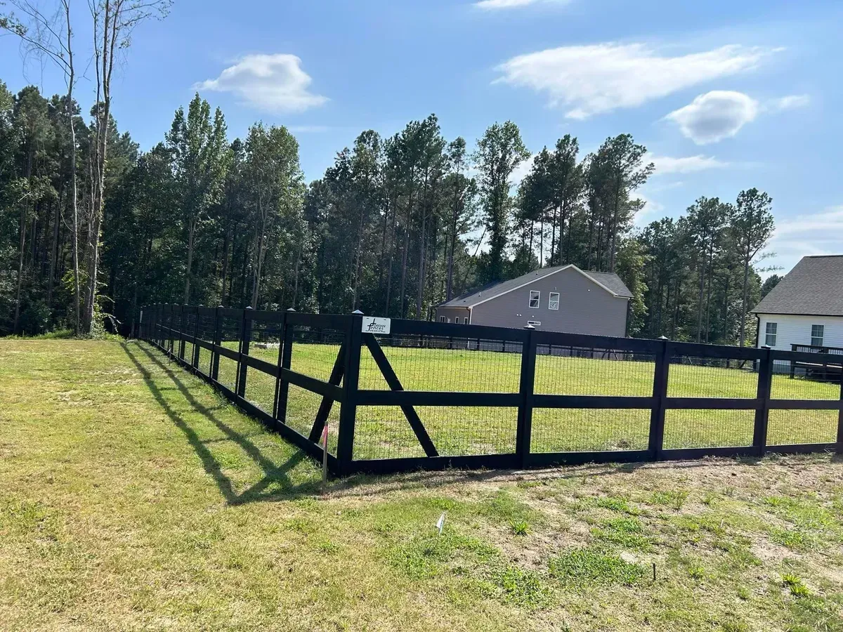 A black fence surrounds a grassy field with a house in the background.