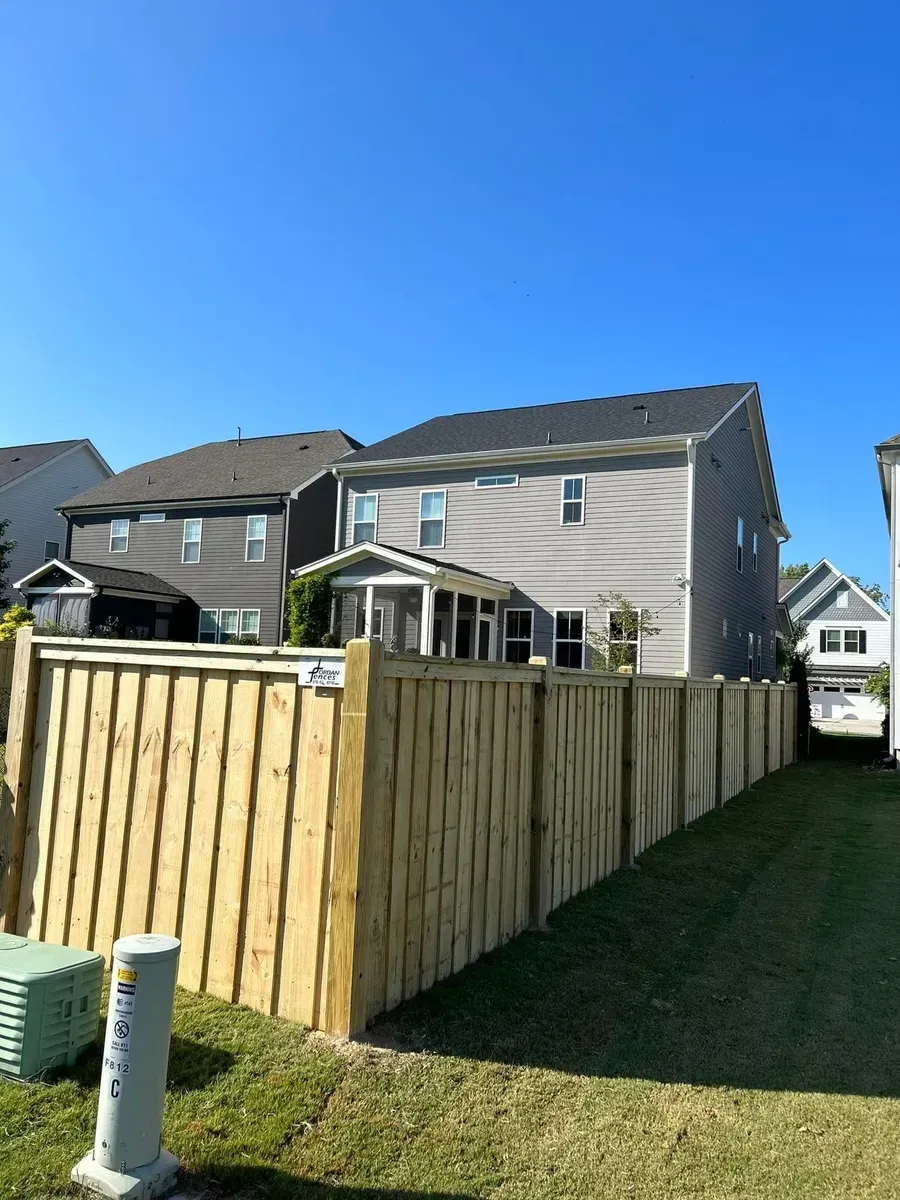 A wooden fence surrounds a lush green yard in front of a house.