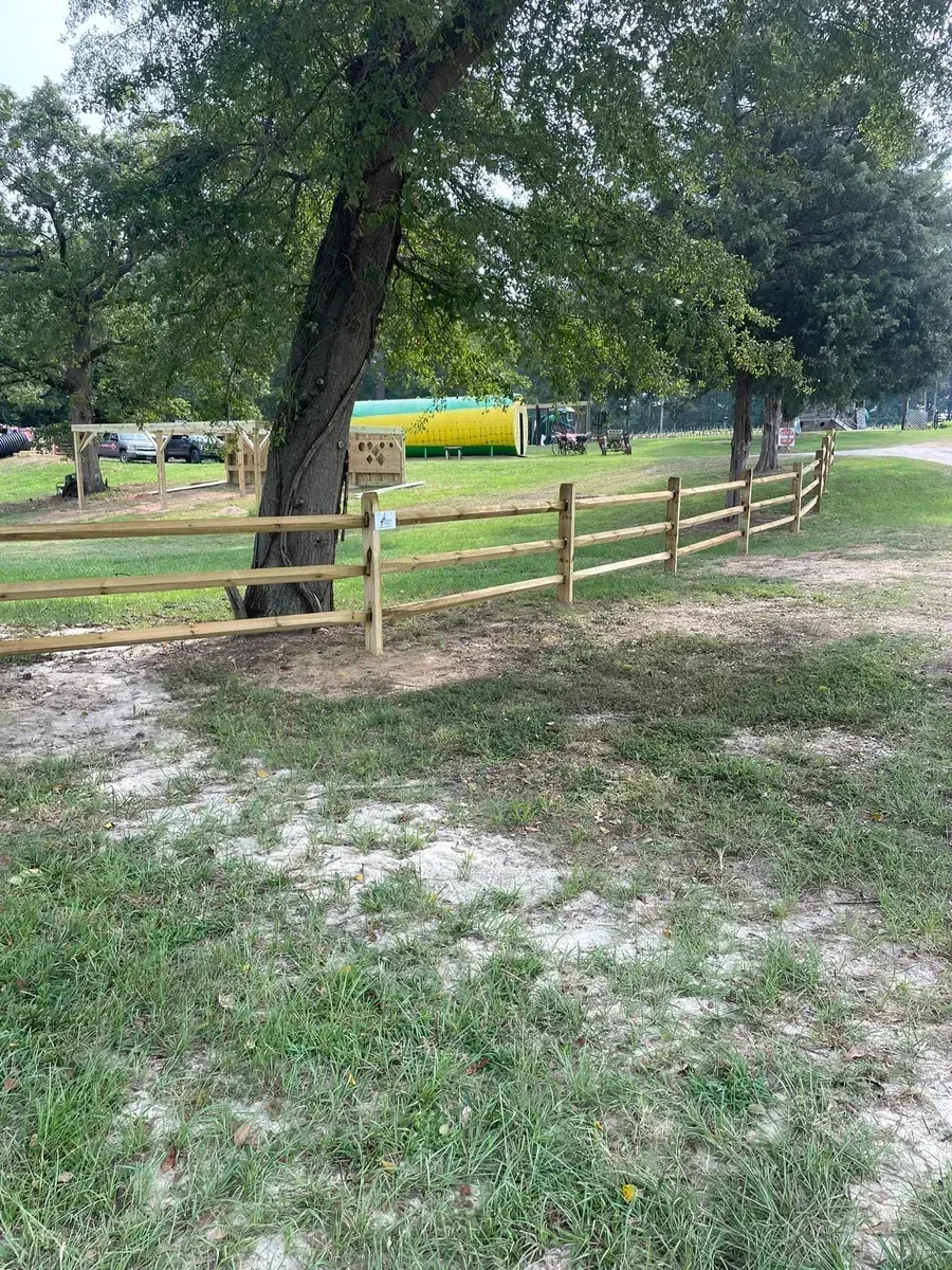 A wooden fence is surrounded by grass and trees in a park.