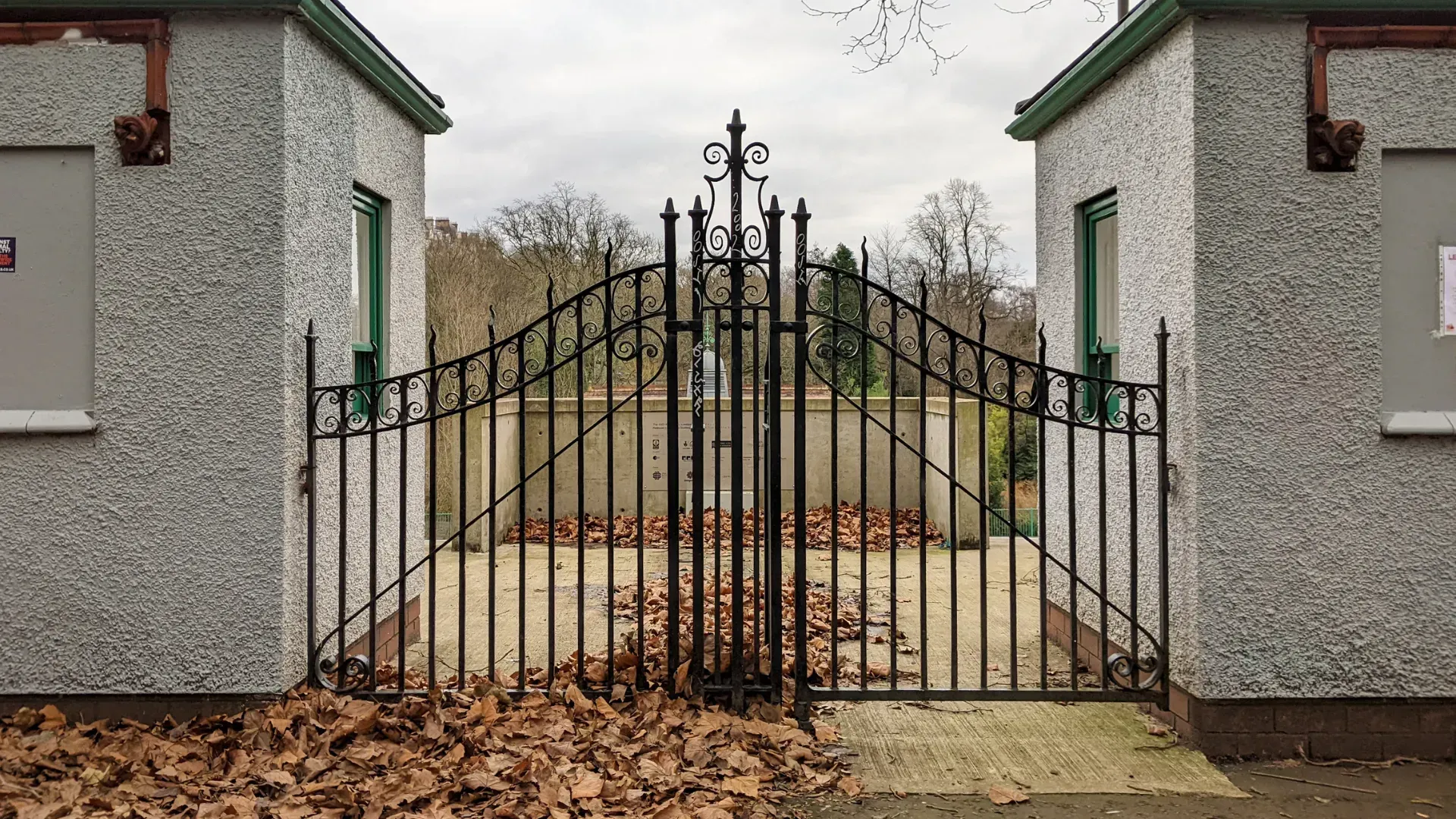 A wrought iron gate is surrounded by leaves on the ground.