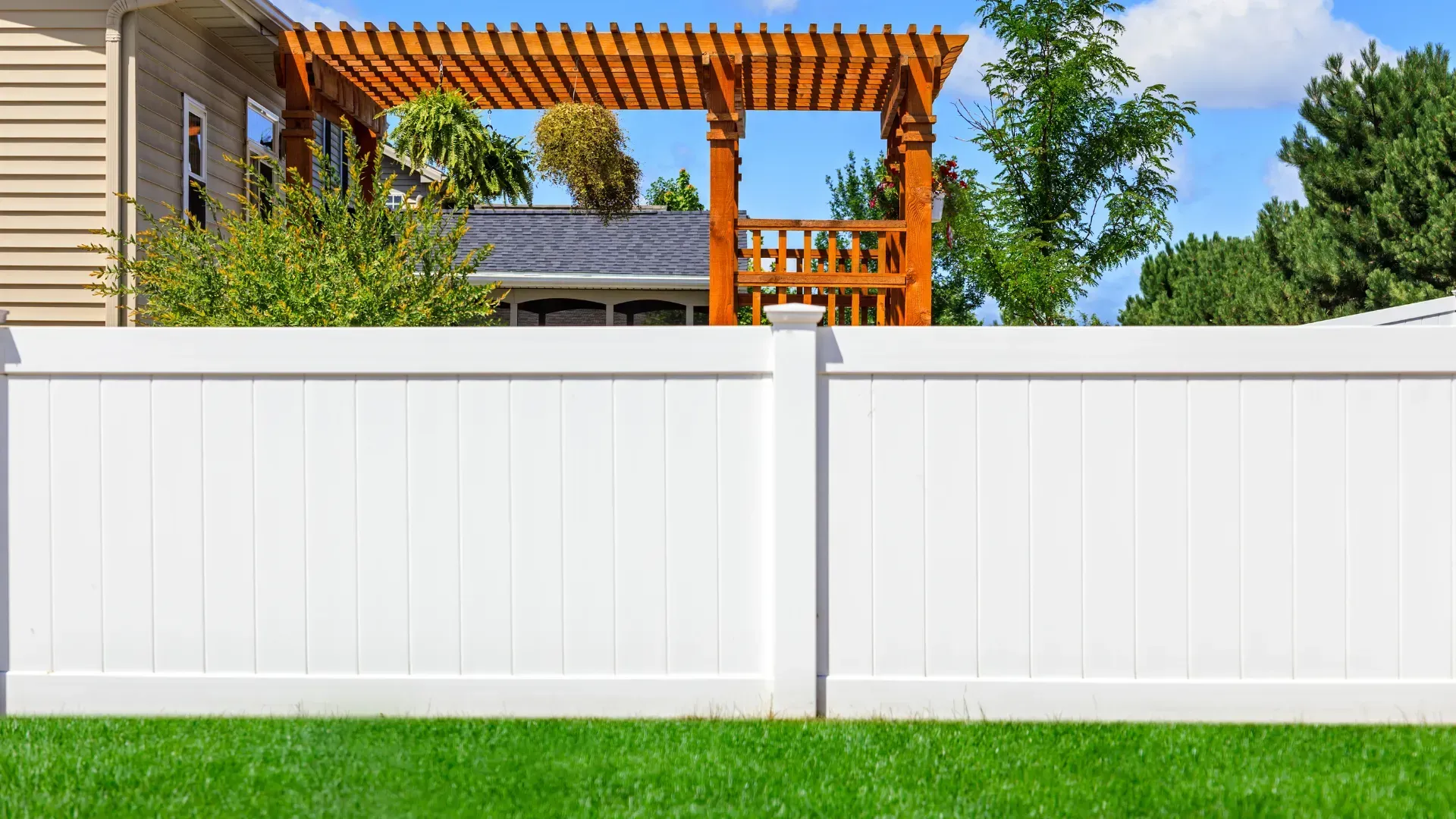 A white fence with a wooden pergola in the backyard of a house.