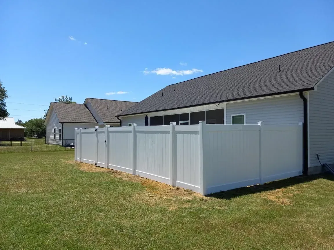 A white fence is in the backyard of a house.