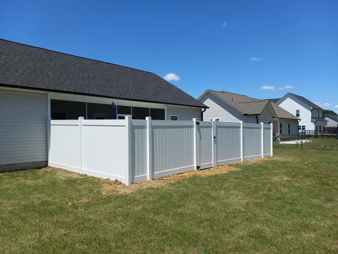 A white fence is in the backyard of a house.