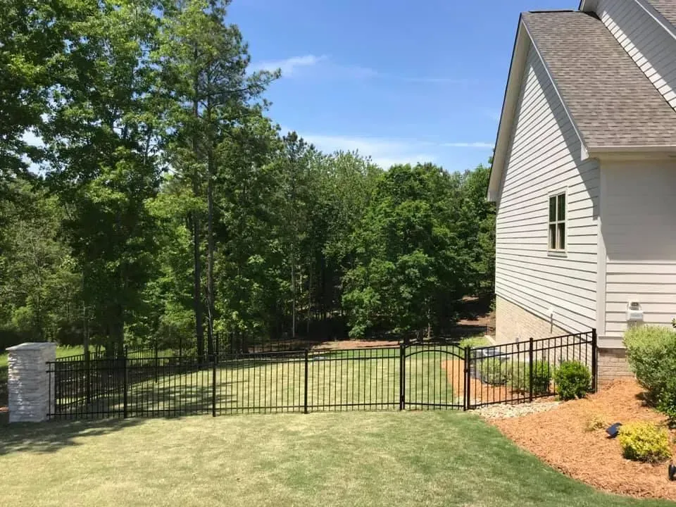 A house with a fence in front of it and trees in the background.