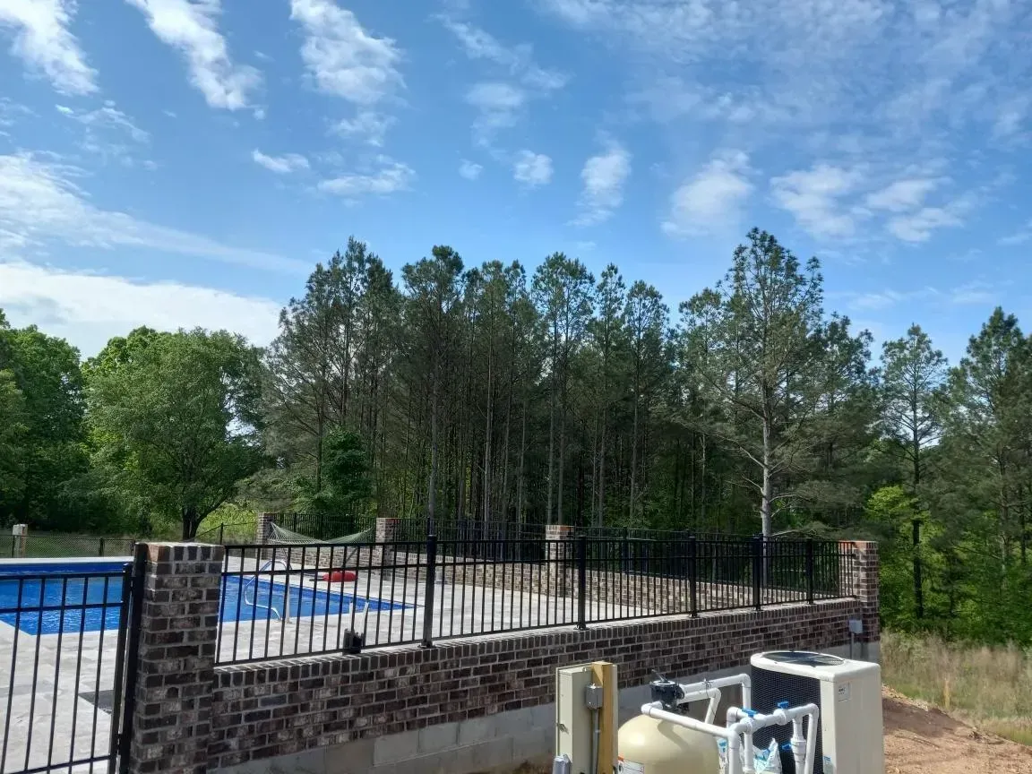 A fence surrounds a swimming pool with trees in the background
